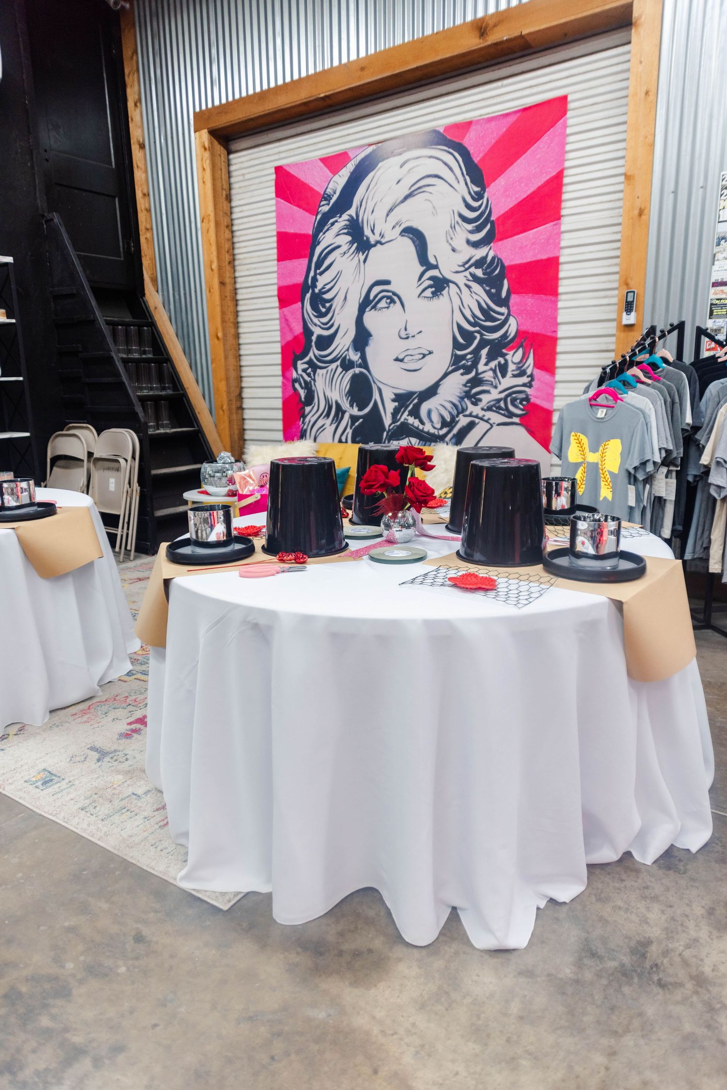 A table set with white linens and black place settings beneath a bold pink and white pop art style portrait on the wall.