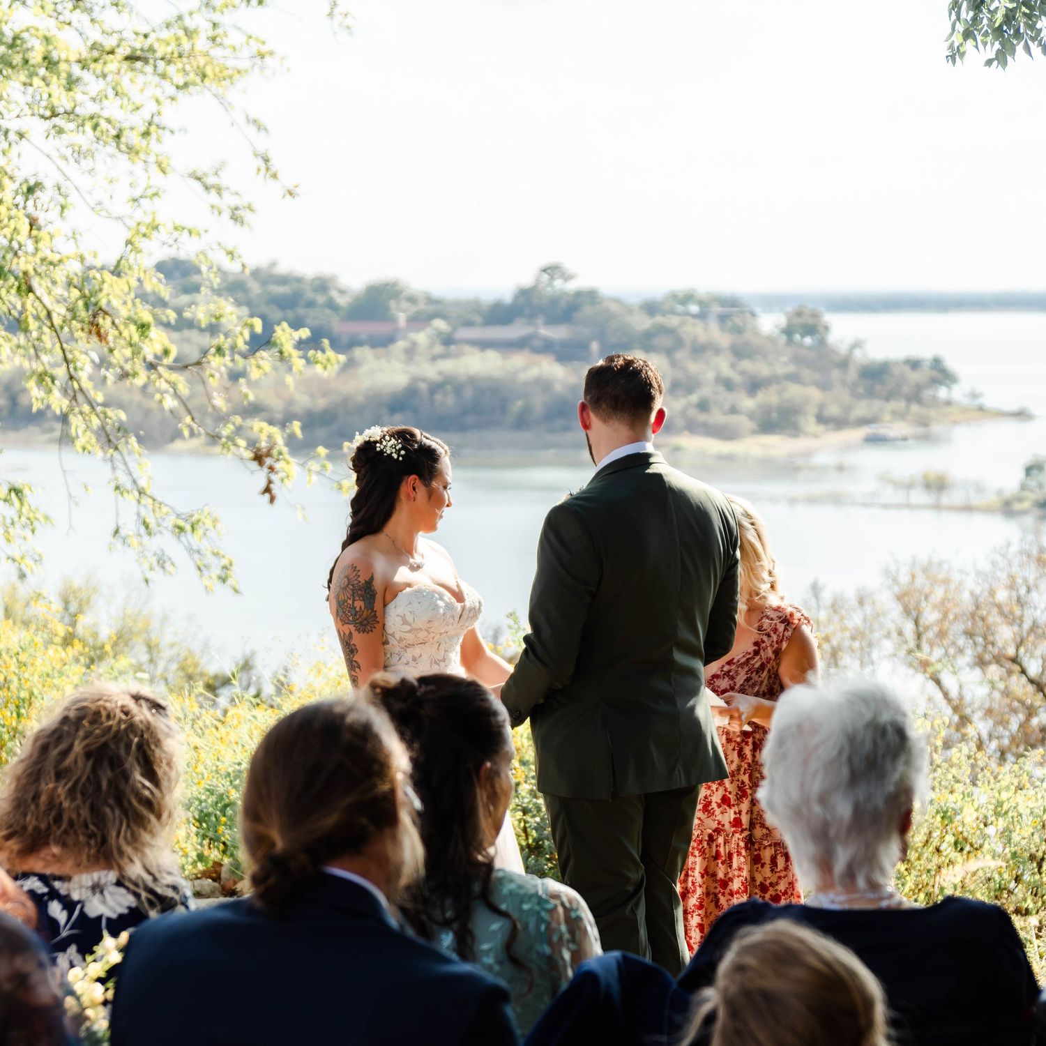 A wedding ceremony overlooking a scenic lake view with guests seated on chairs and greenery in the background.