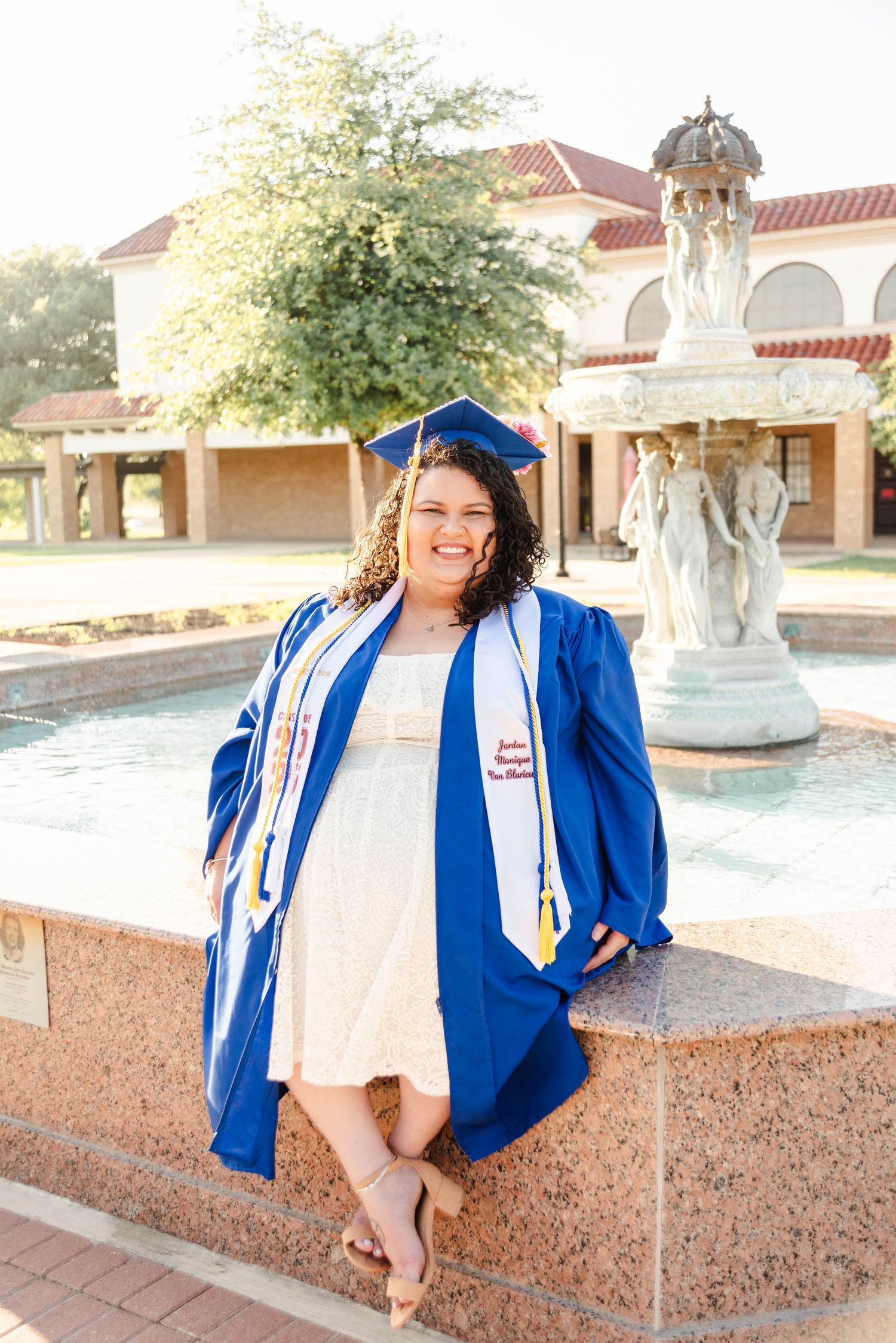 a female sitting at a fountain with her cap and gown on