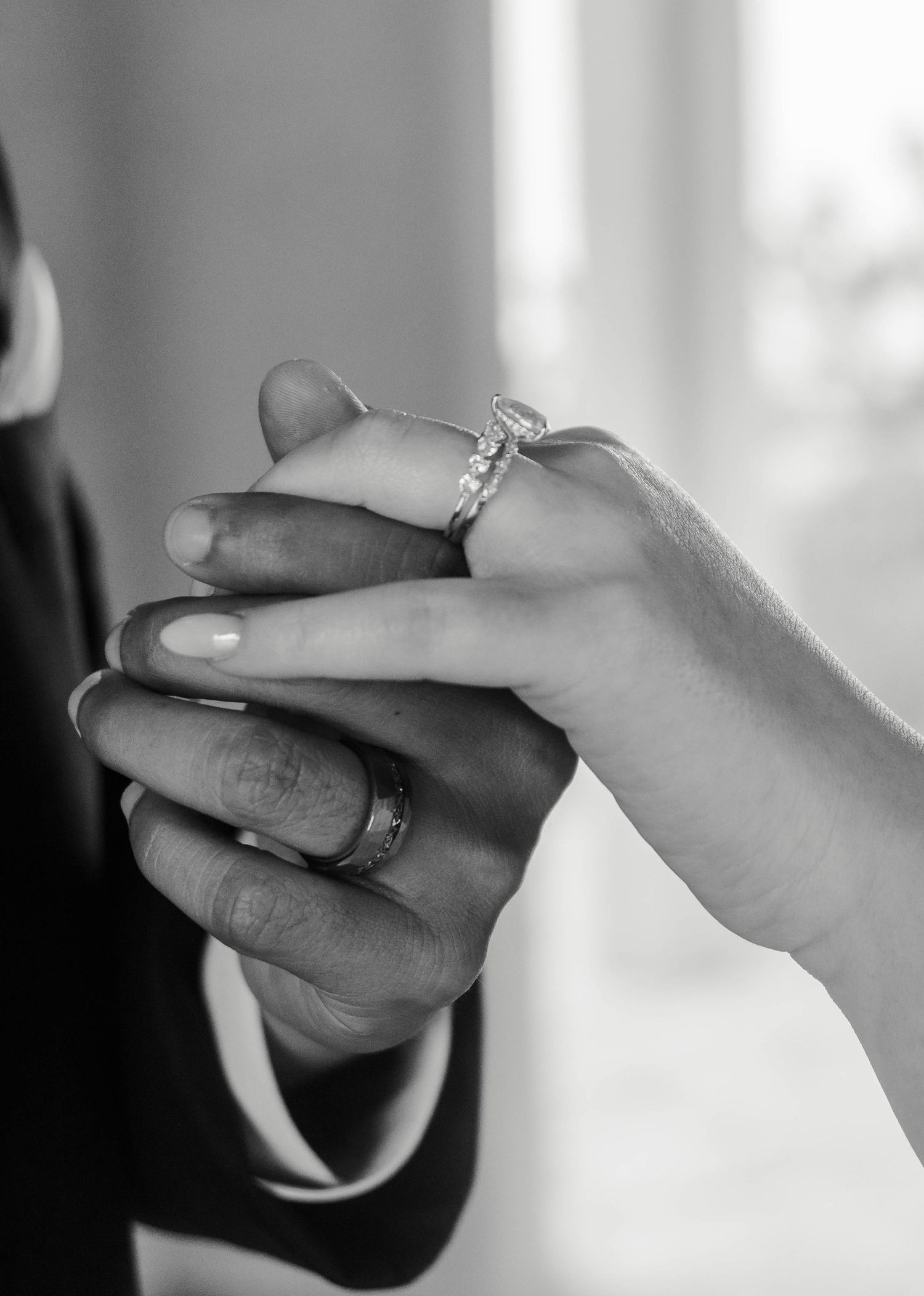 Black and white close-up of two hands with wedding rings held together in an intimate moment.