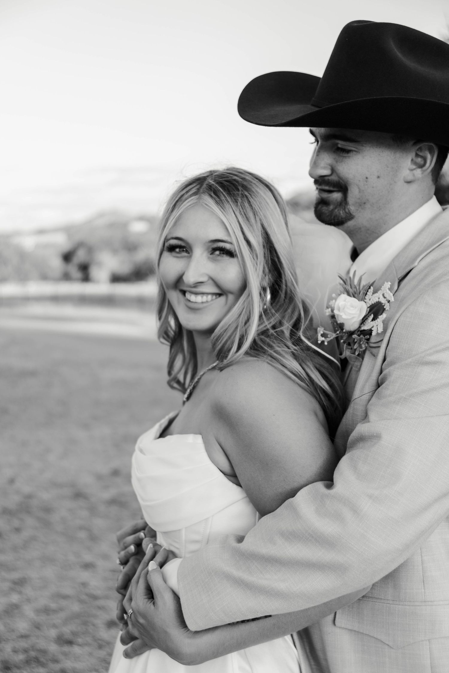 Black and white wedding photo showing romantic embrace between couple in western attire outdoors.
