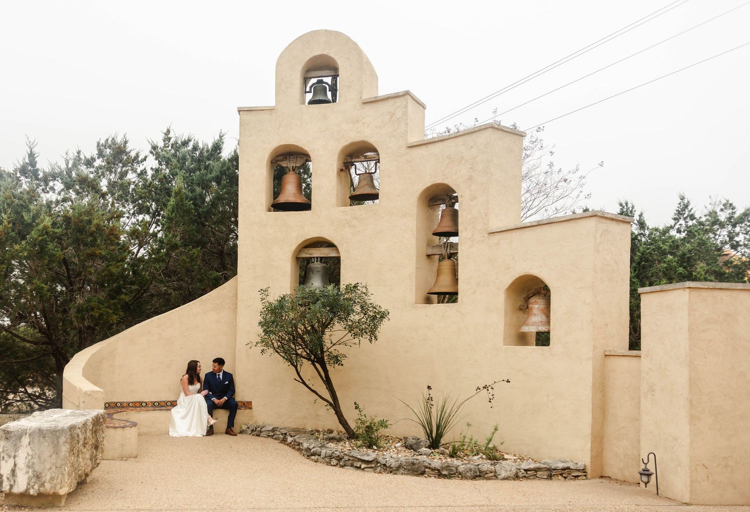 a couple sits together under a bell tower wall