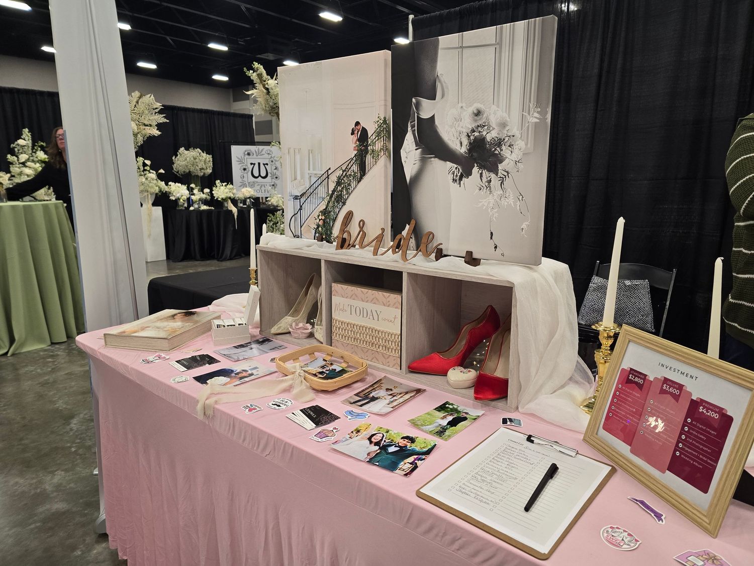 Wedding vendor booth at a bridal show with pink tablecloth displays photos, books and decorative elements.