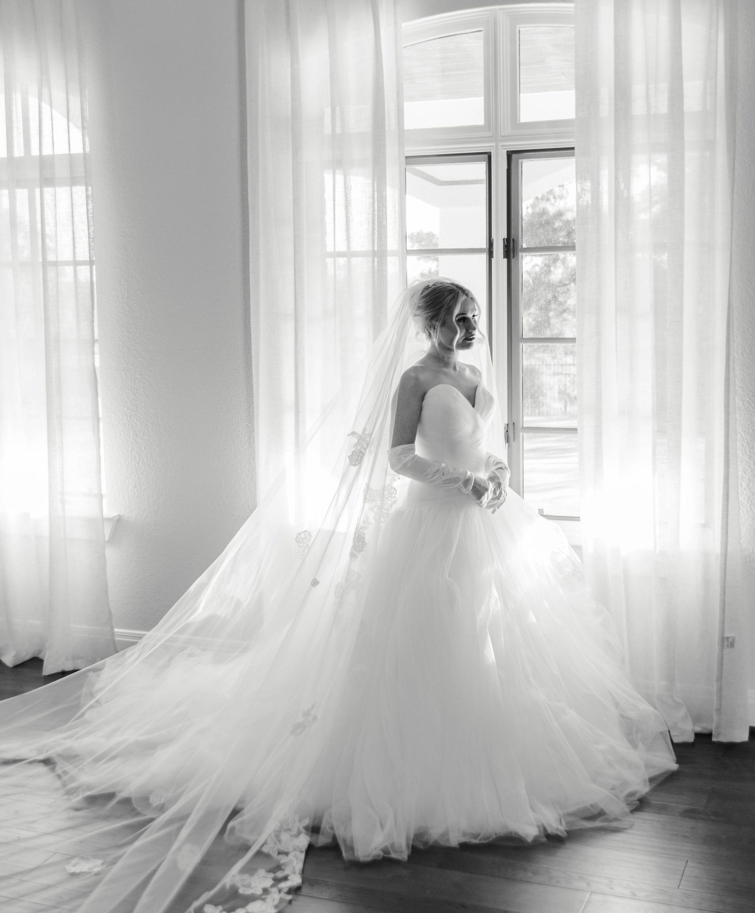 bride in her dress and veil standing waiting by a window