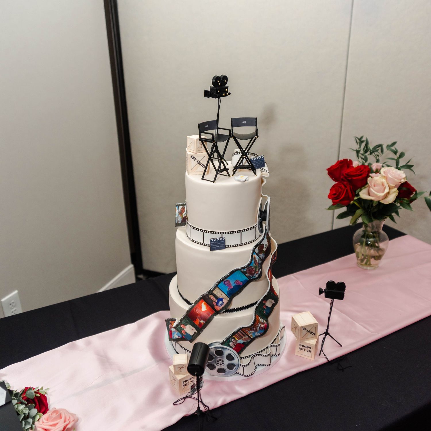 A cake that is movie themed with director's chairs, a film reel, film strips, and staging equipment