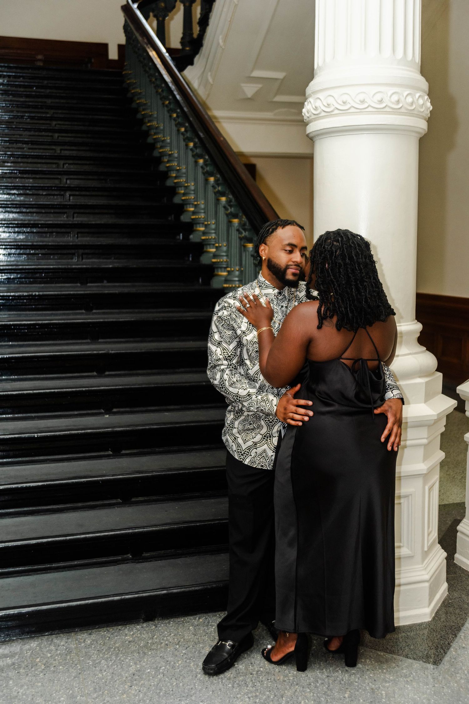 A couple stands looking lovingly to each other inside the state Capitol Building near the stairs