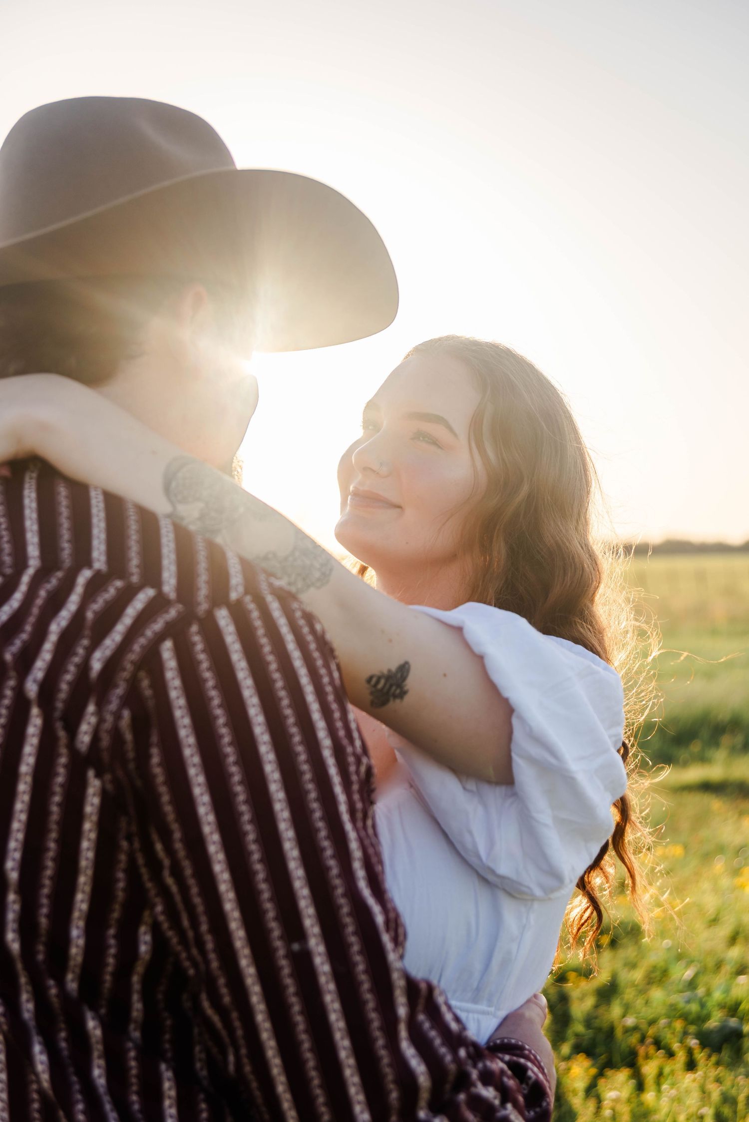 woman and man standing in a field together looking up at each other as the sun sets between them
