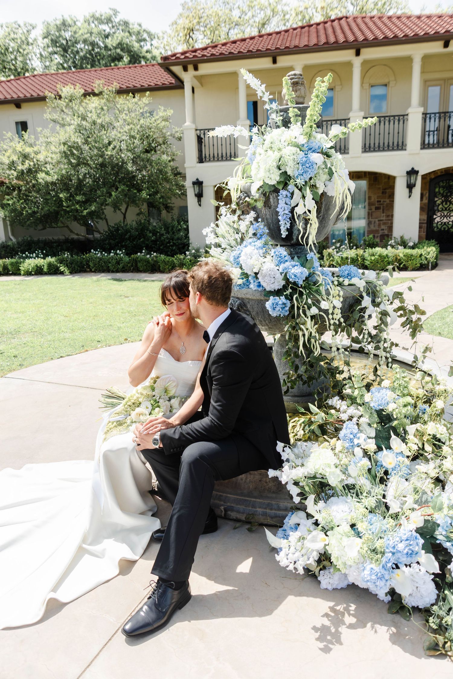 A couple sitting at the fountain together while the groom kisses the bride's cheek