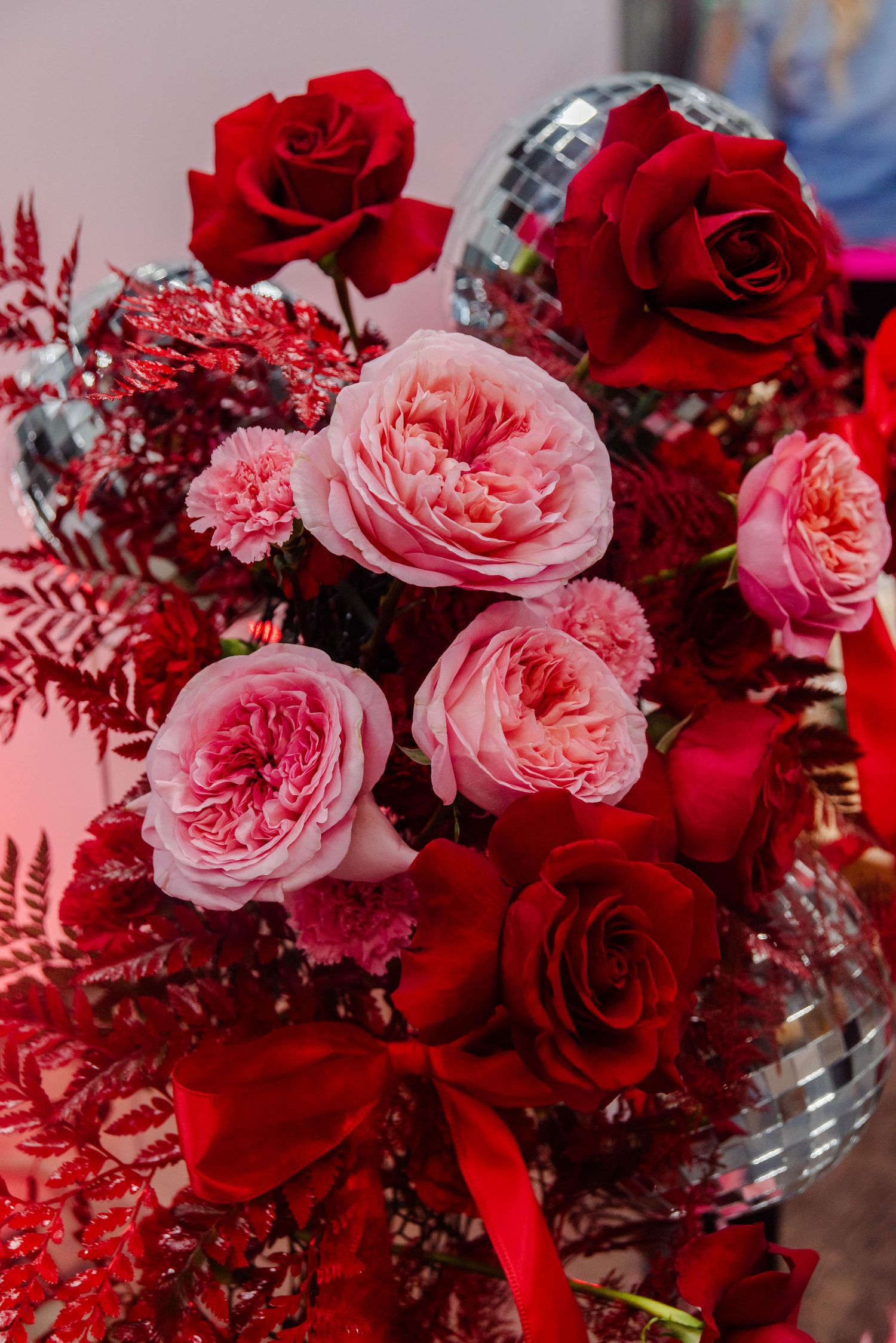 A romantic floral arrangement featuring pink garden roses and deep red roses with red accents and glittering silver details.