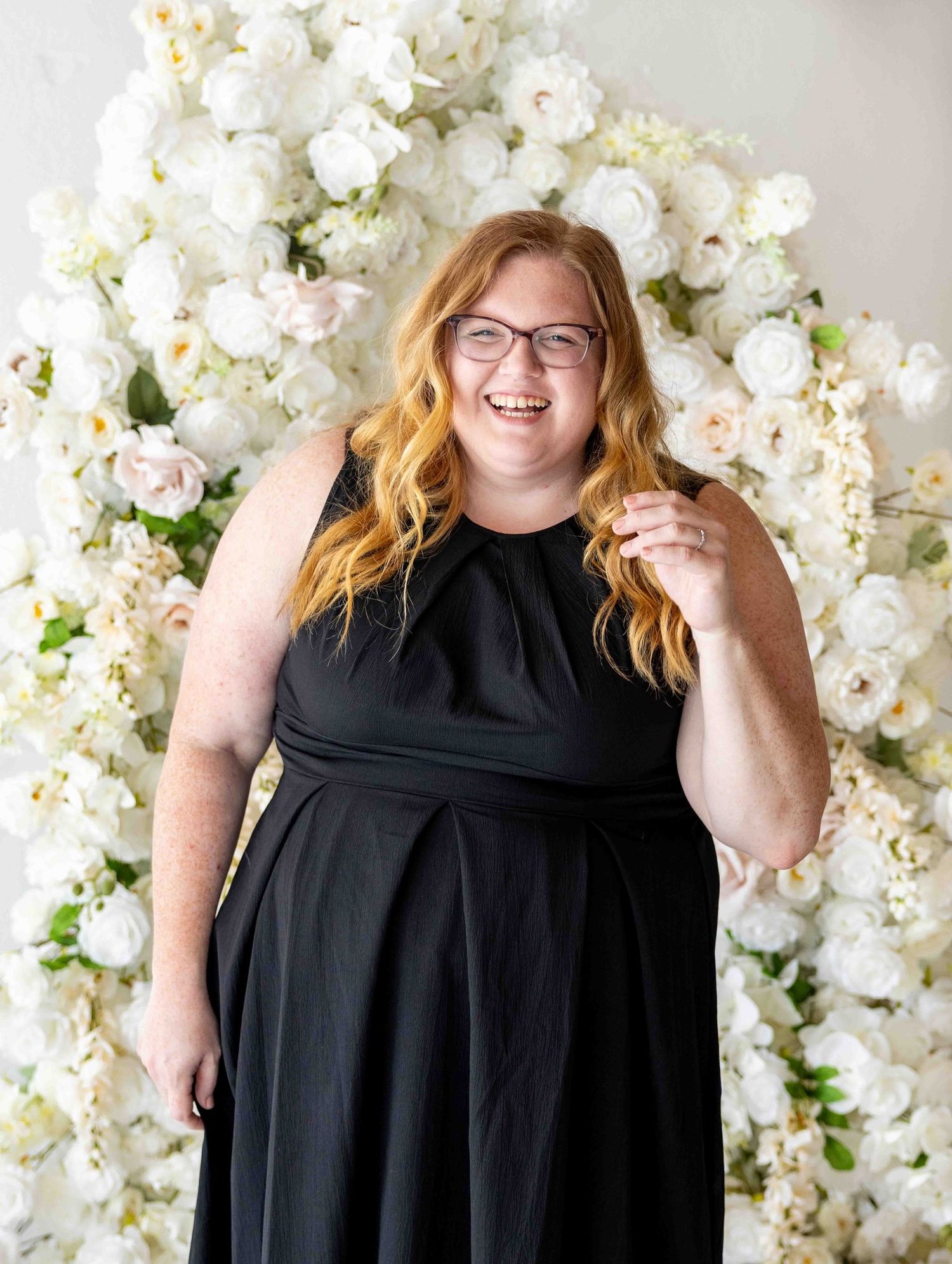 Cerria from Cerria Maryann Photography in a black dress and laughing in front of florals