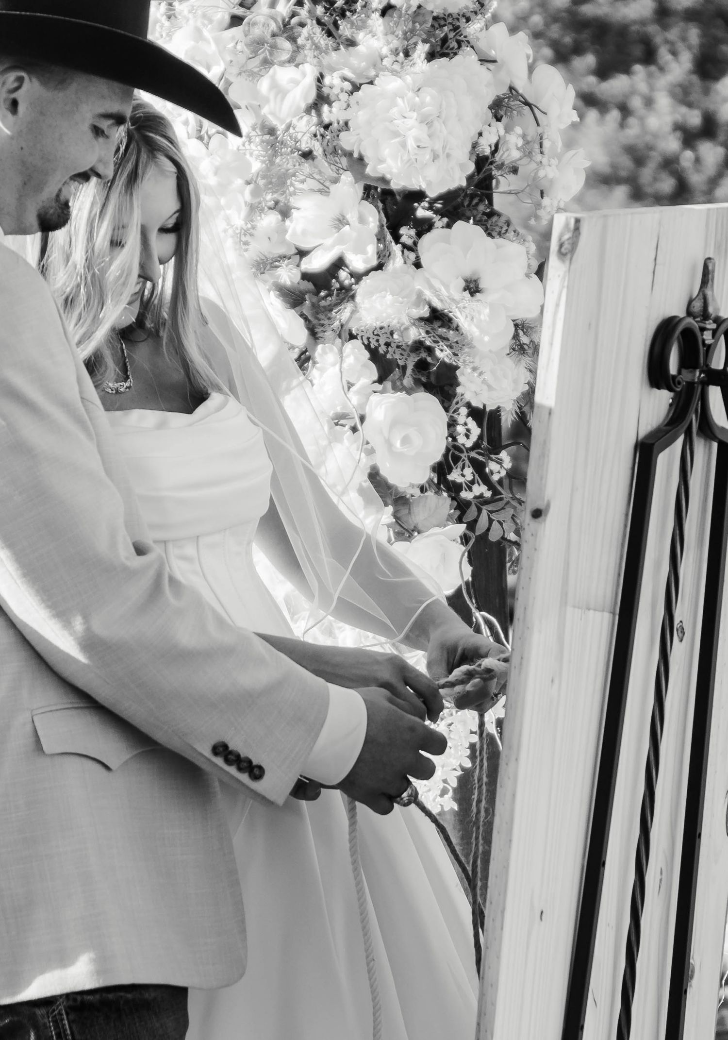 A romantic black and white wedding photograph showing a couple embracing next to elegant floral decorations.