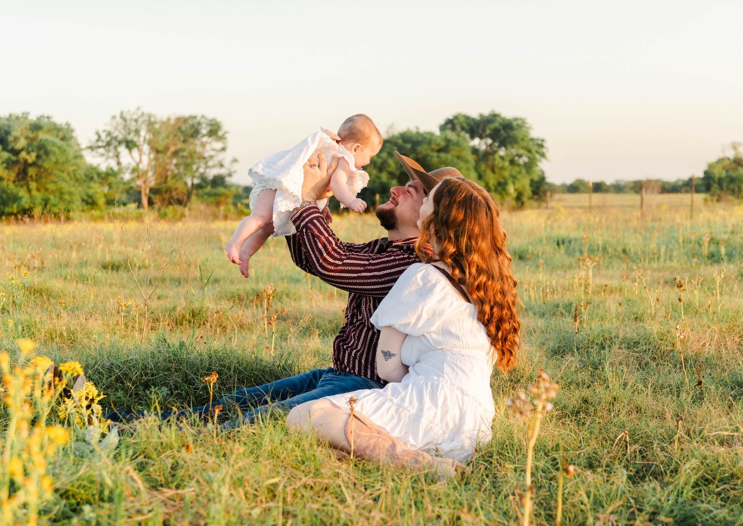 the man is holding the baby up playing with the baby as the woman leans in and looks up towards the baby