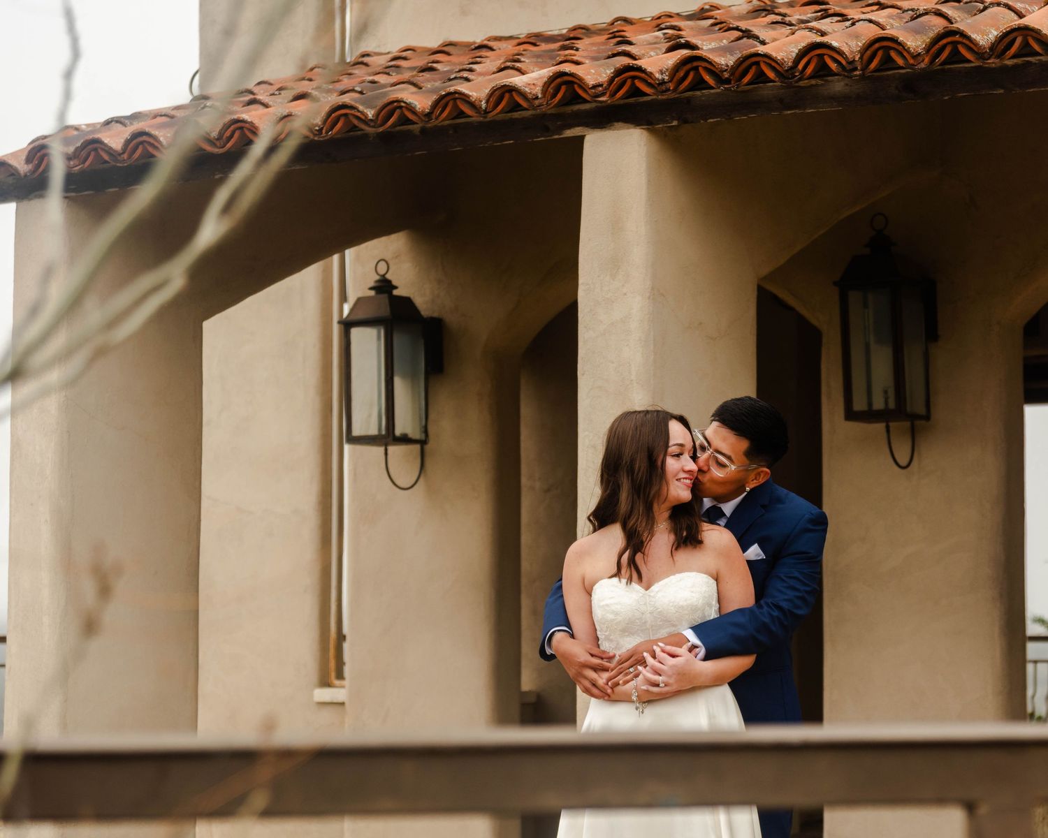 A romantic moment shared between a couple embracing on a Spanish-style terrace with rustic lanterns on the walls.