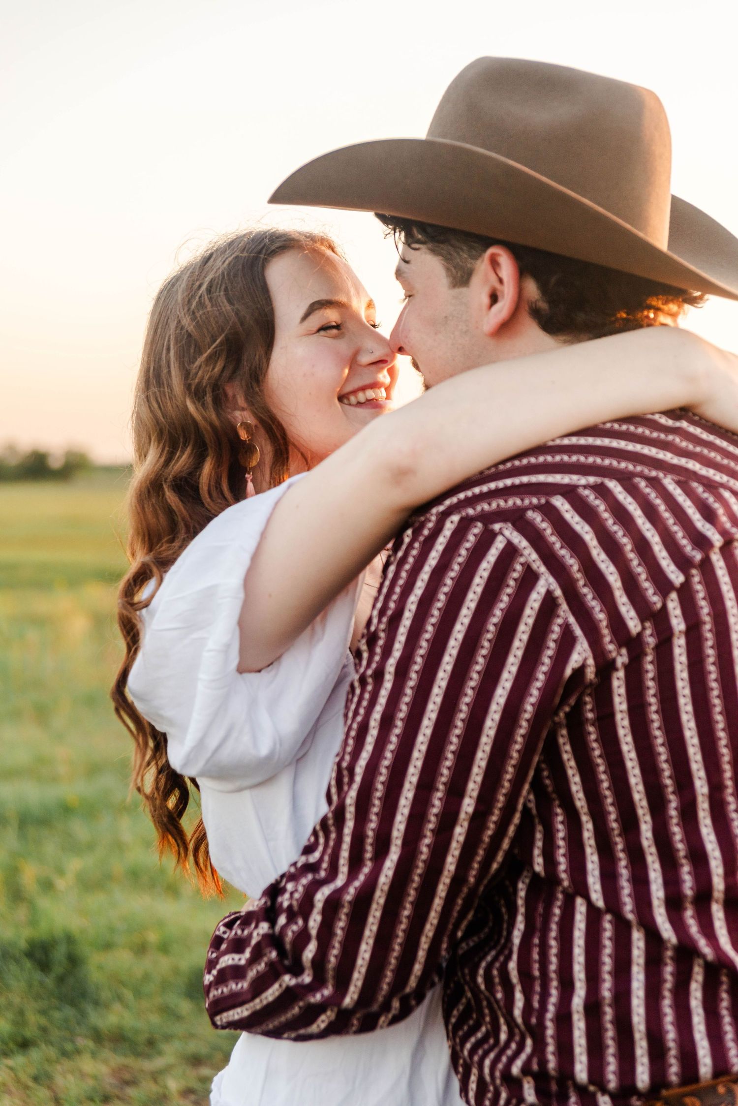 couple is smiling at each other while hugging in an open field at sunset