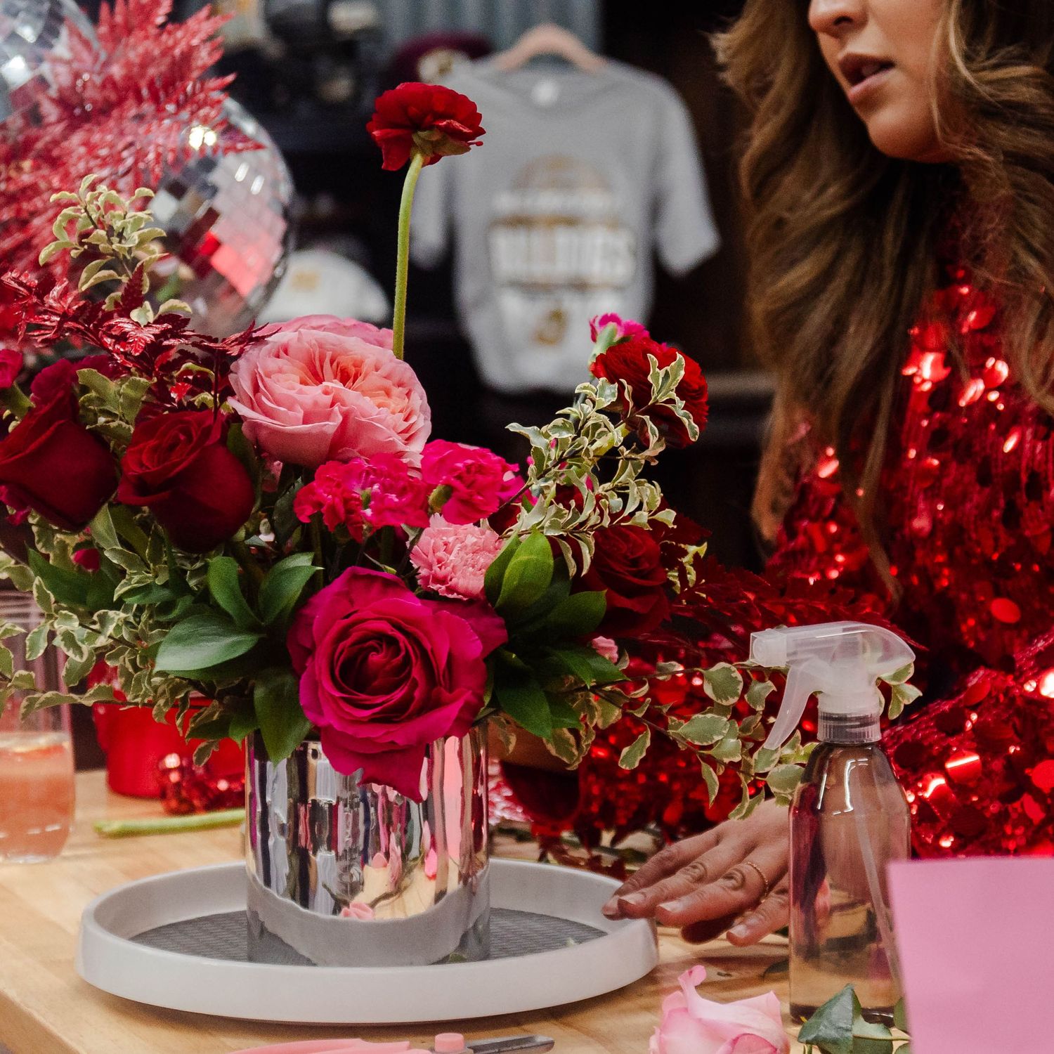 Beautiful floral arrangement with pink and red roses in a modern vase alongside festive red decor on a table setting.