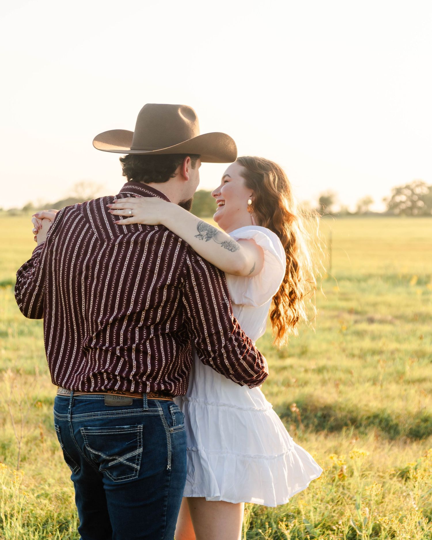 couple is dancing and laughing in a pasture wearing western attire