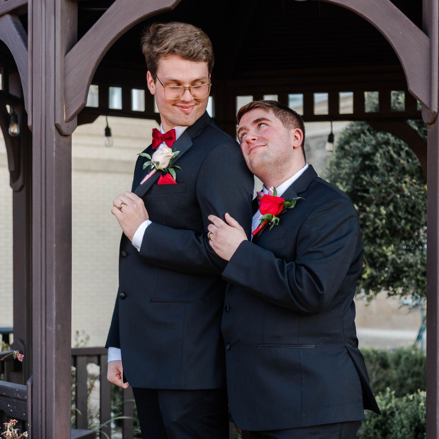 A gay couple standing in a gazebo looking at each other lovingly and smiling
