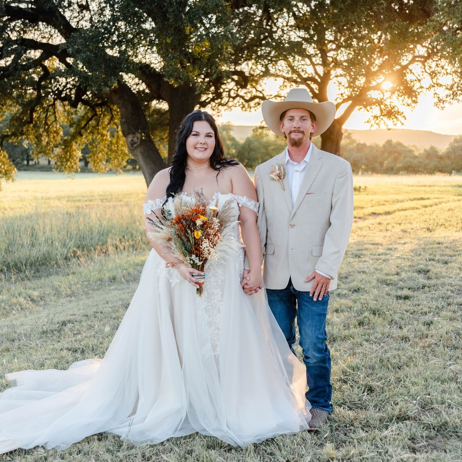 couple standing in a field in wedding attire at with a golden sunset filtered through the trees