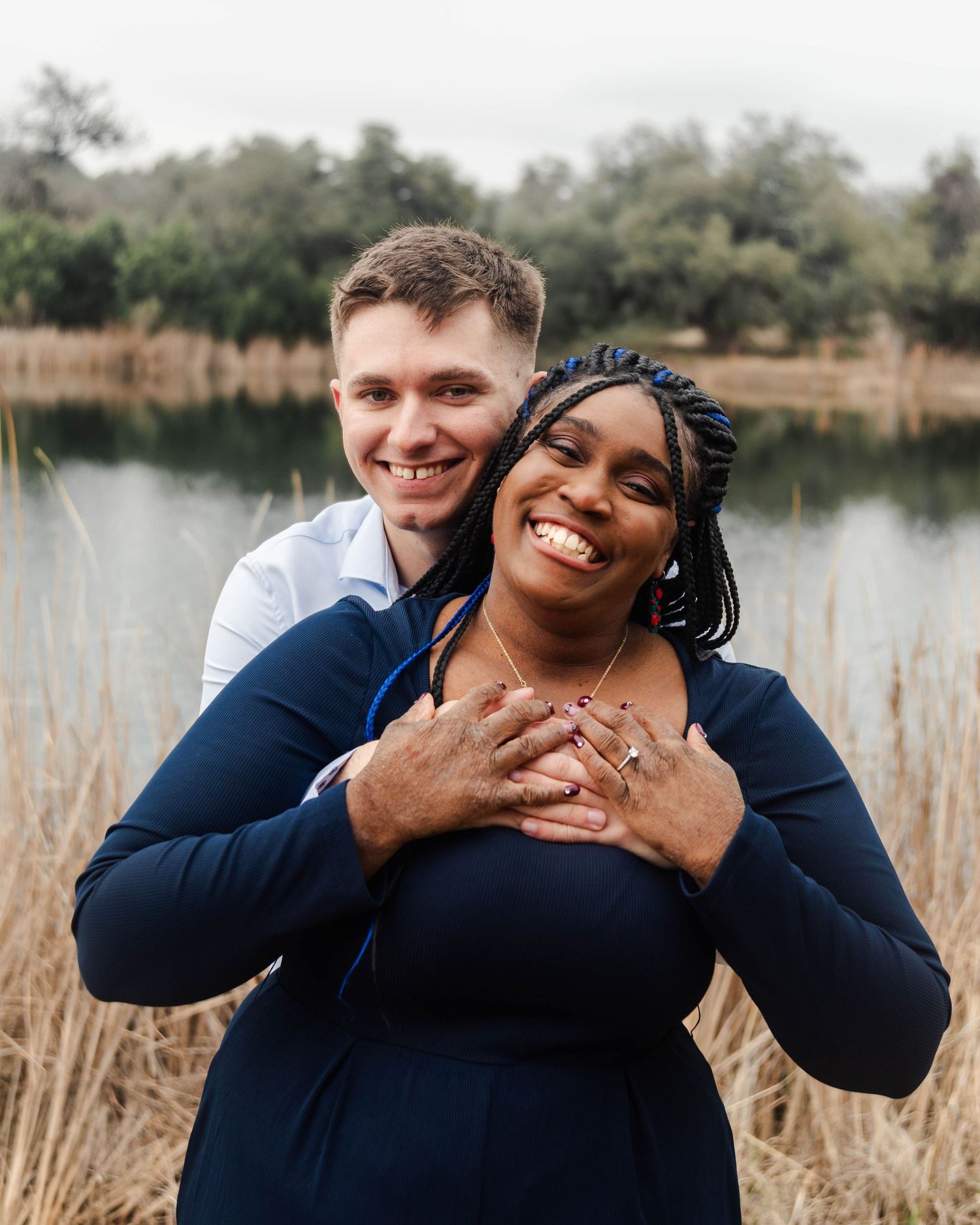 a couple smiling in front of a pond with tall grass
