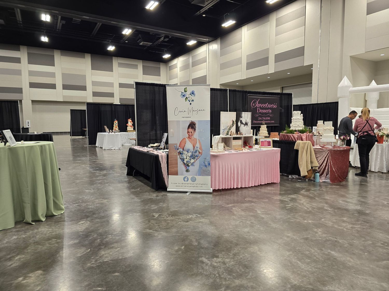 Small vendor booths with displays set up in a convention center hall with concrete floors and white walls.