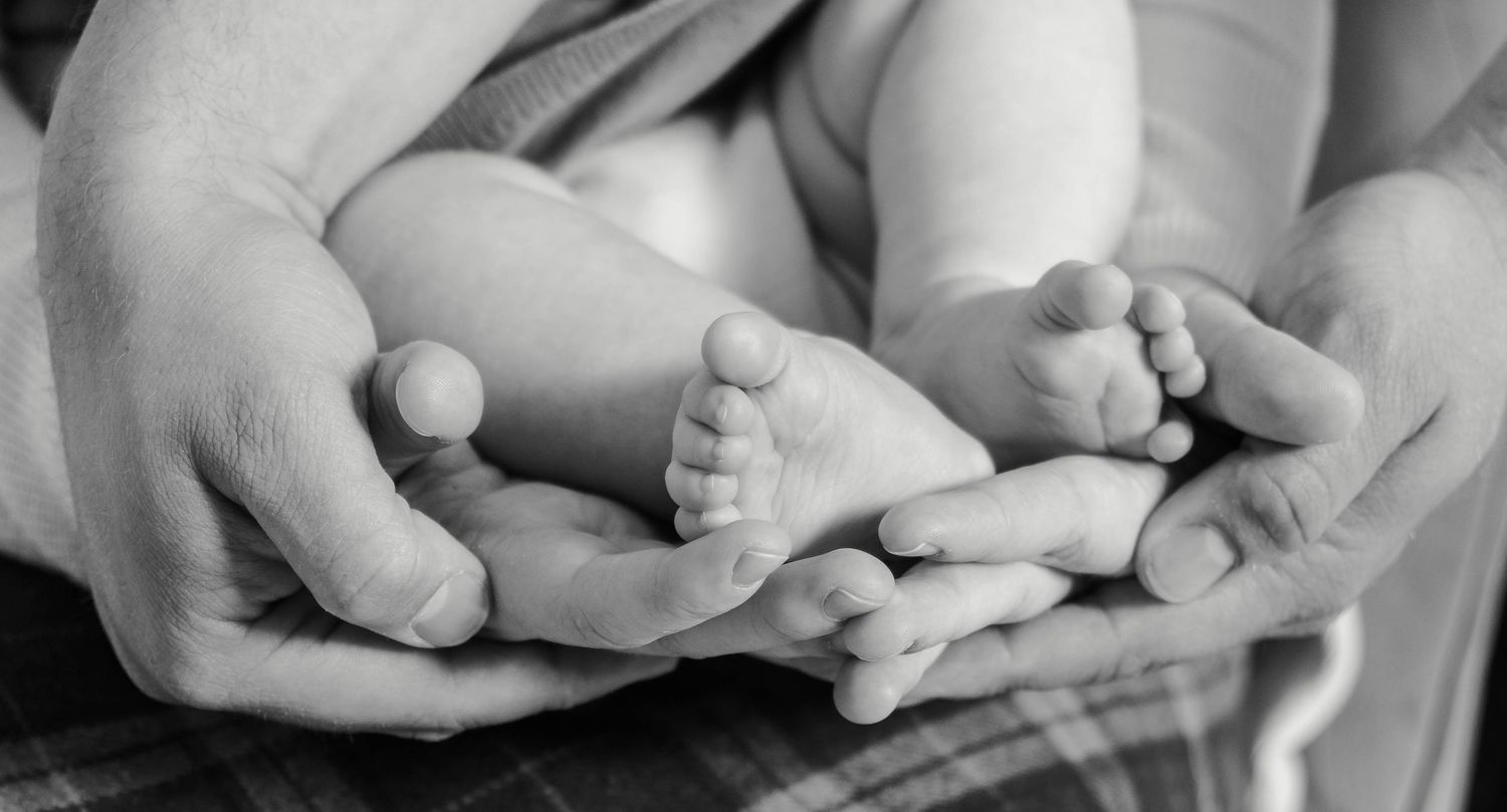 A family holds their hands around the baby's feet