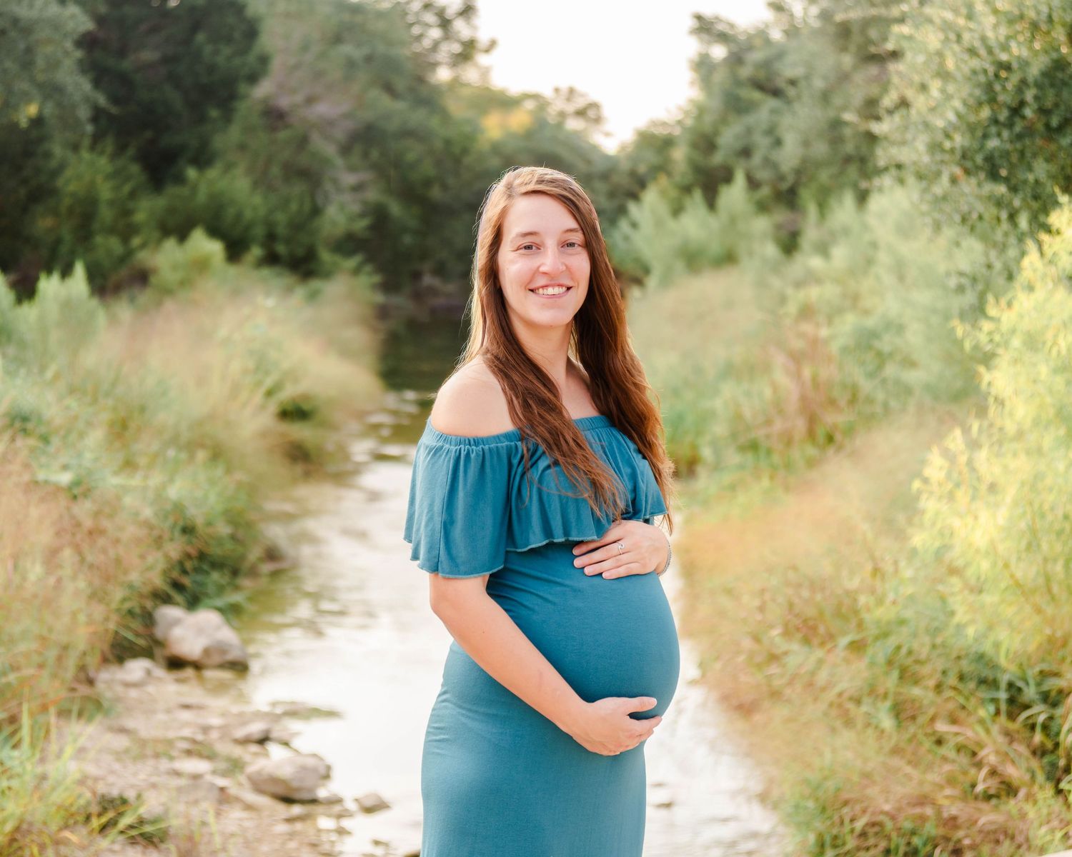 A lady holds her maternity belly while smiling