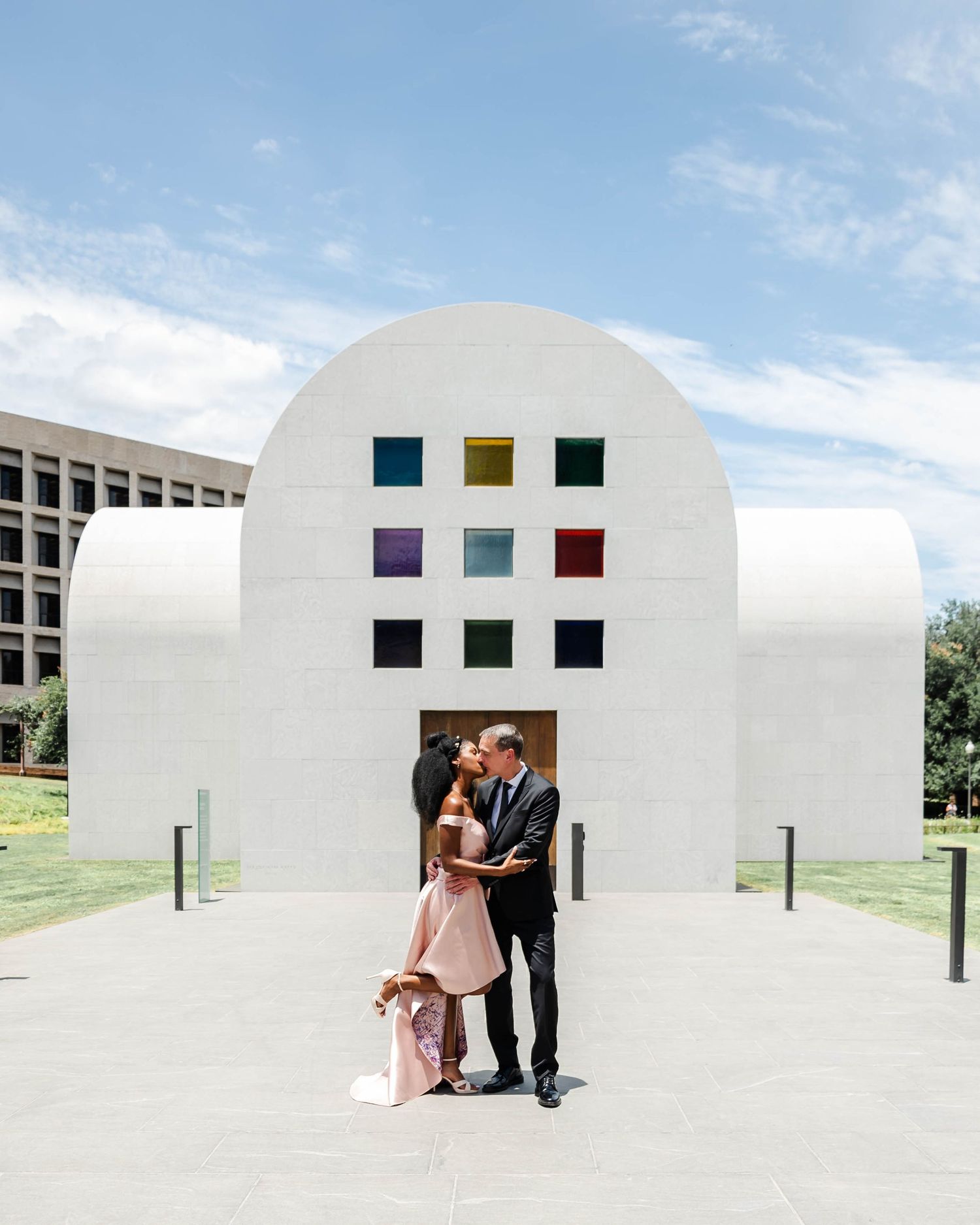 A couple kisses in front of a white chapel with rainbow windows