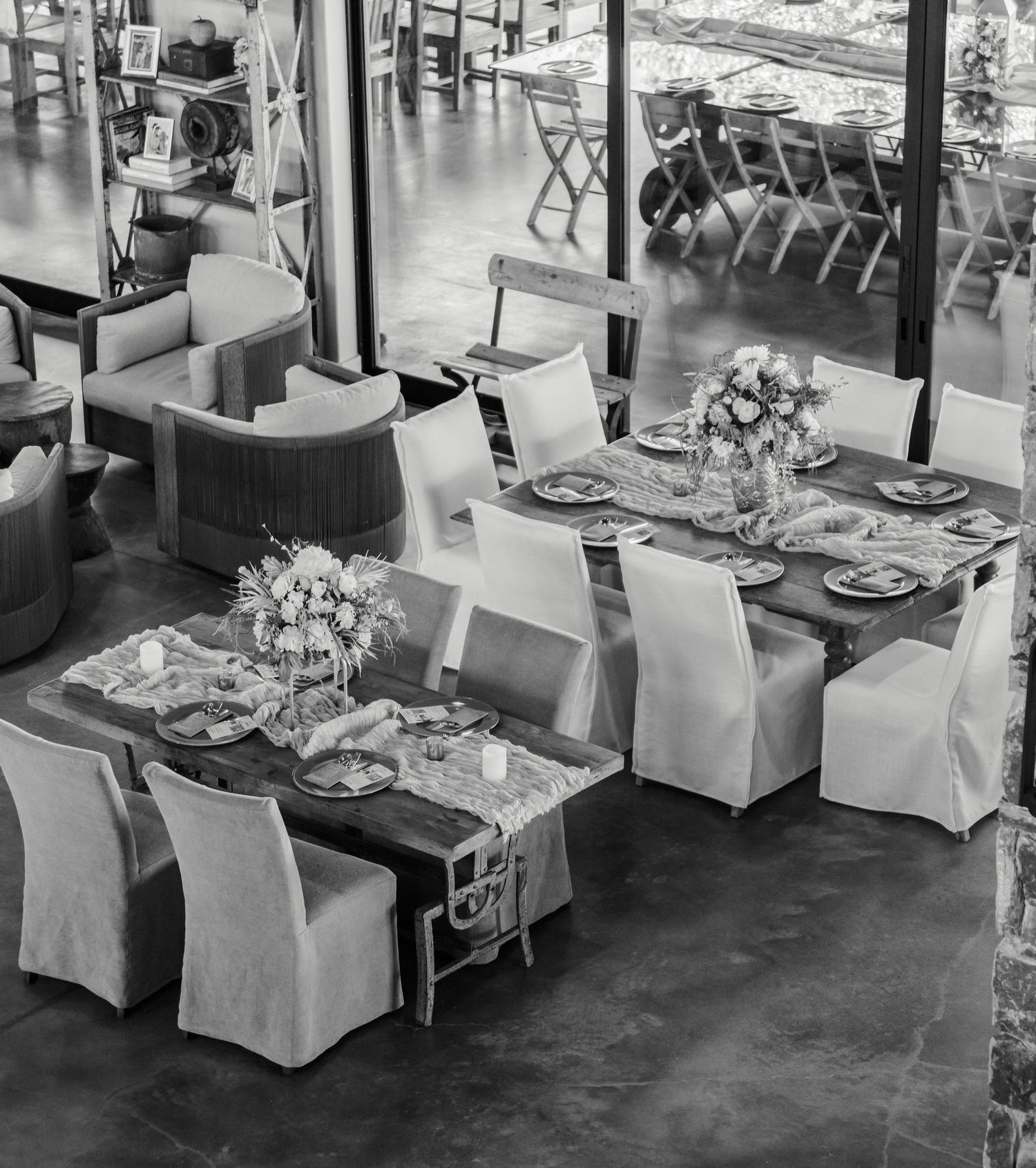An elegant restaurant interior with white chair covers, formal place settings, and fresh floral centerpieces on dining tables.