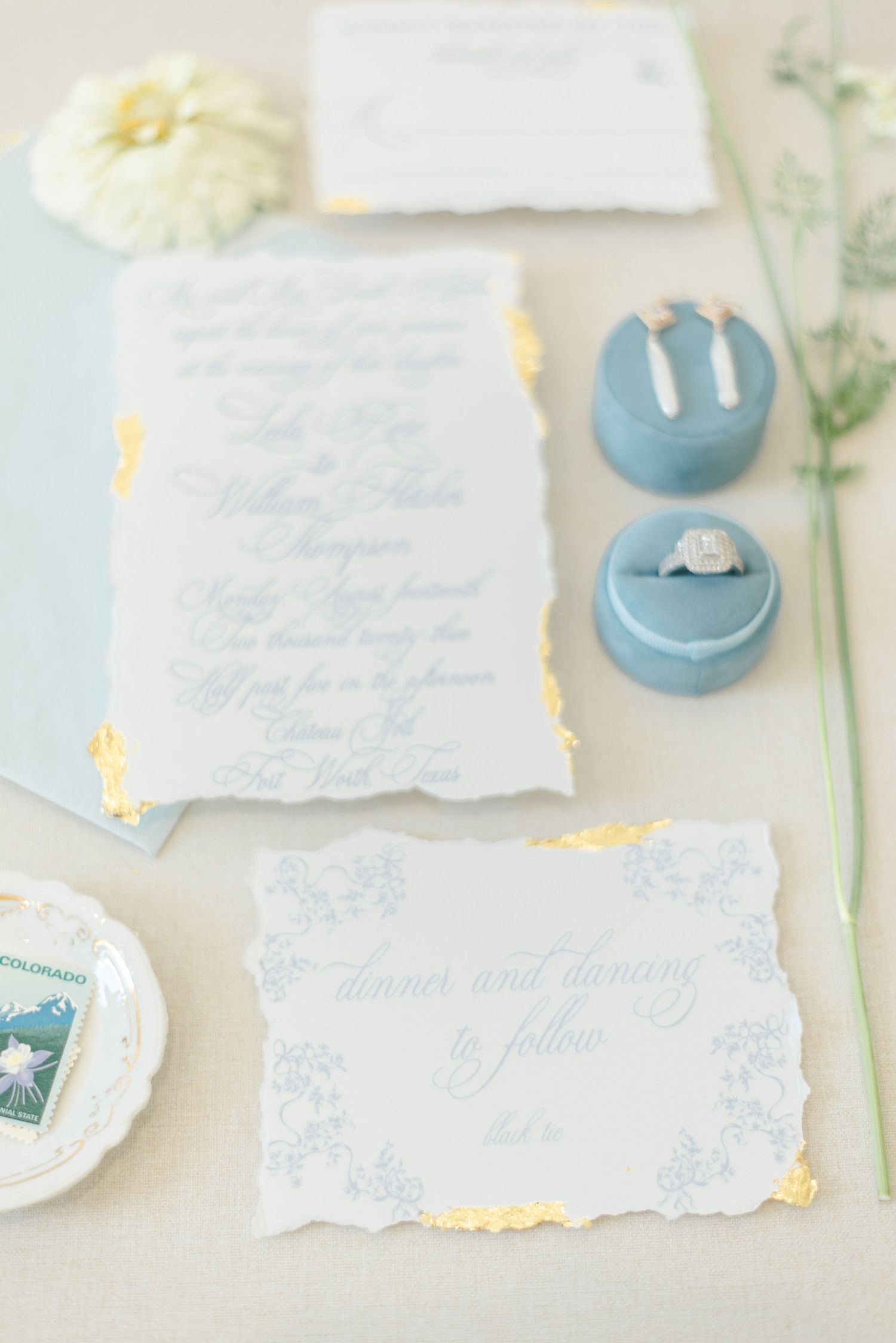 A flatlay with the bride's ring, earrings, wedding invitation set and flowers