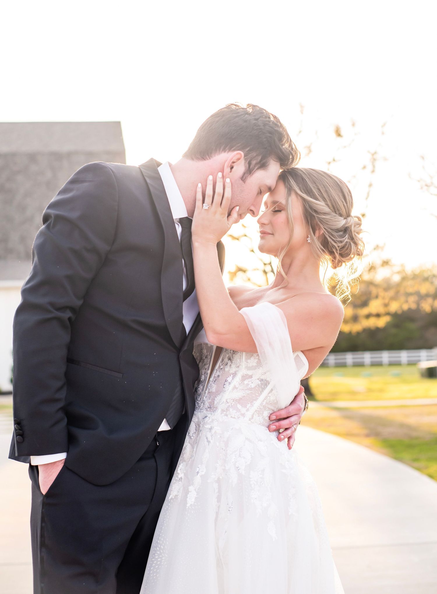 A woman gently touches a mans face as their foreheads touch. They are in a wedding dress and tuxedo