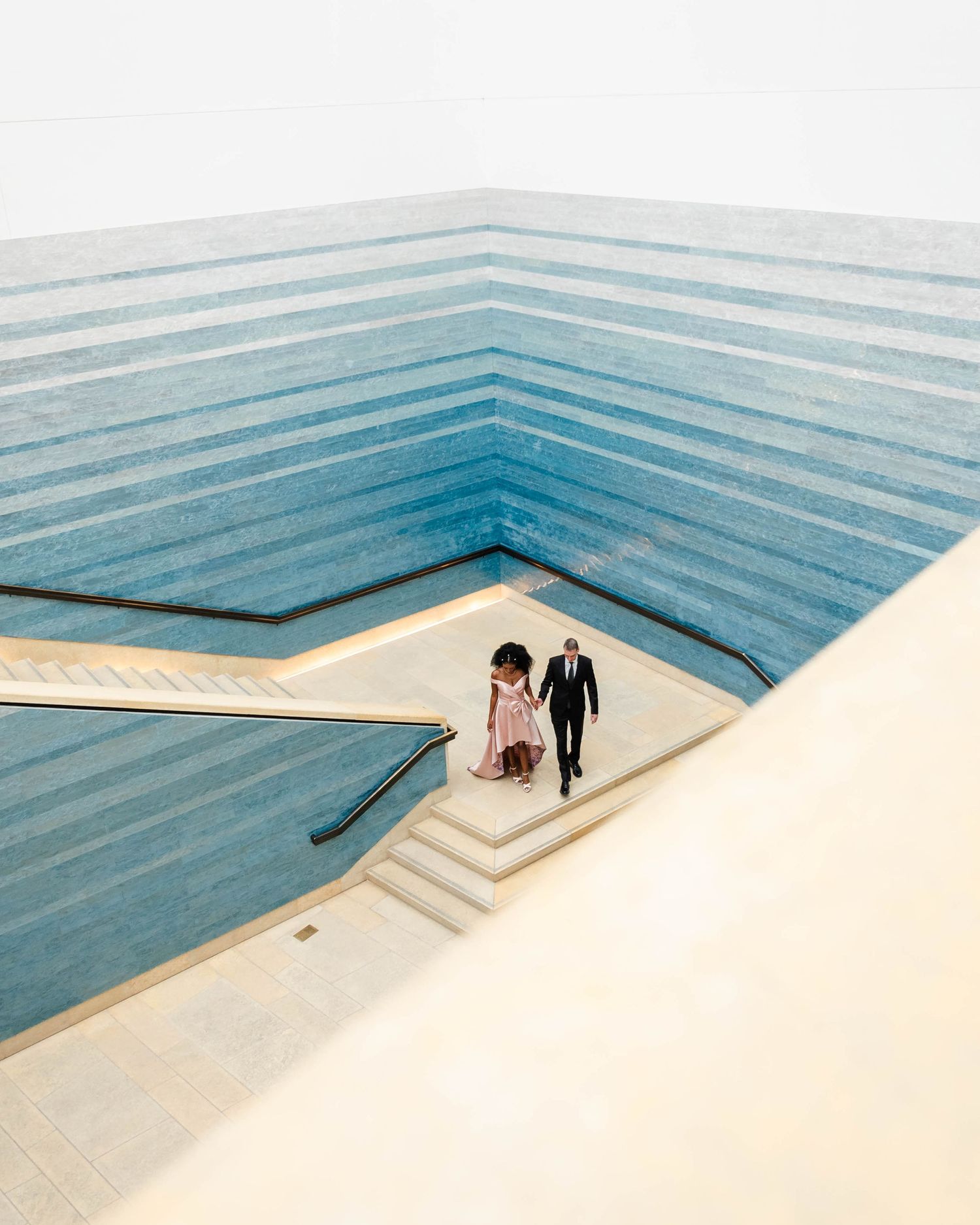 Two small figures descend modern architectural stairs within a geometric blue and white interior space.