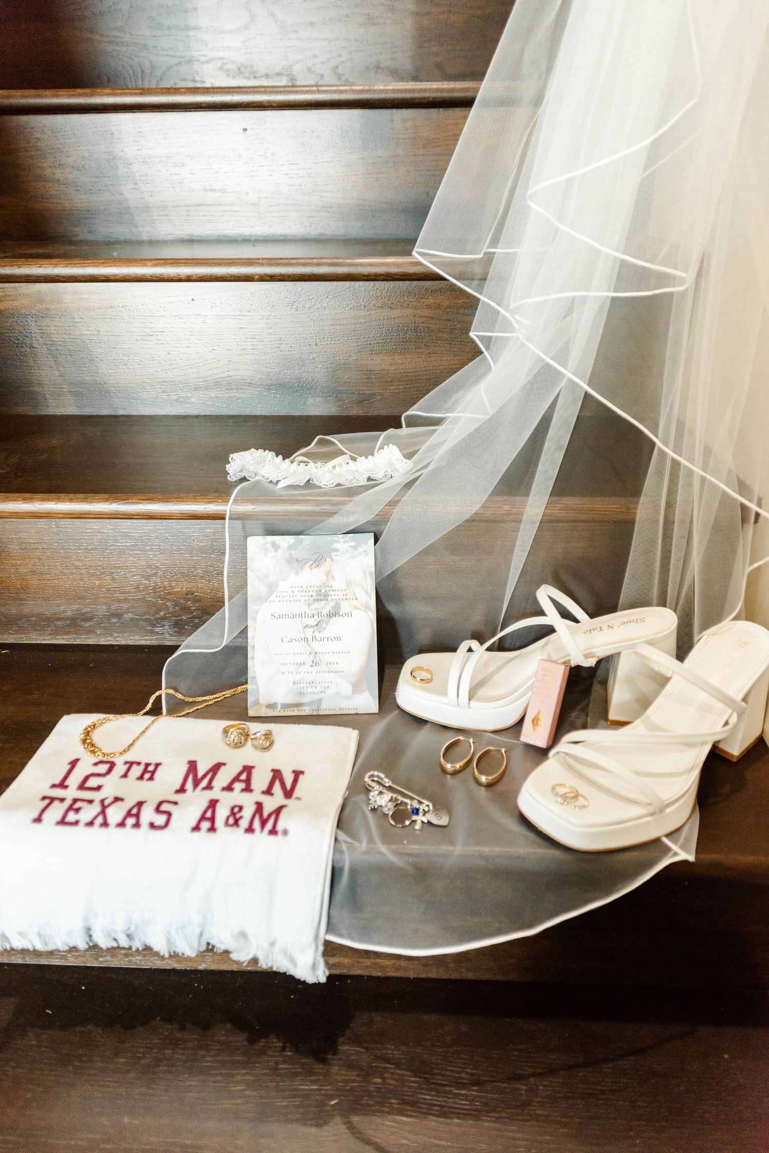 Wedding details including white heels, veil, rings, and Texas A&M 12th Man pillow arranged on wooden stairs.