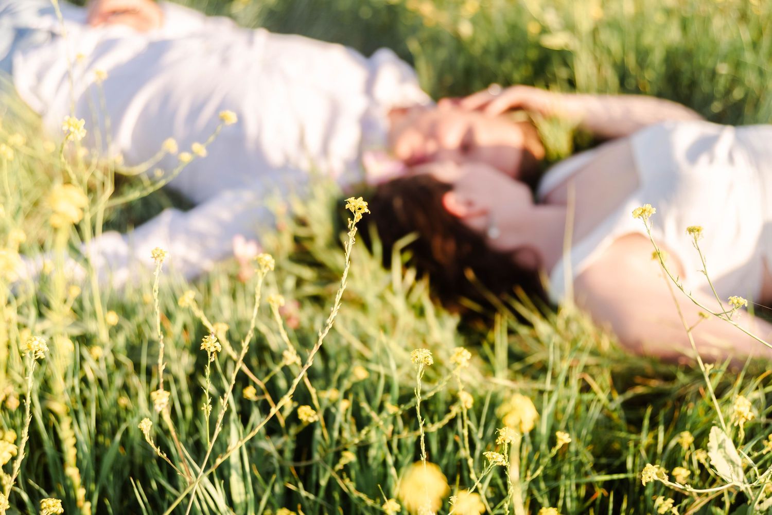 couple is laying in the yellow flowers with the focus being on the flowers as they relax in the sunshine