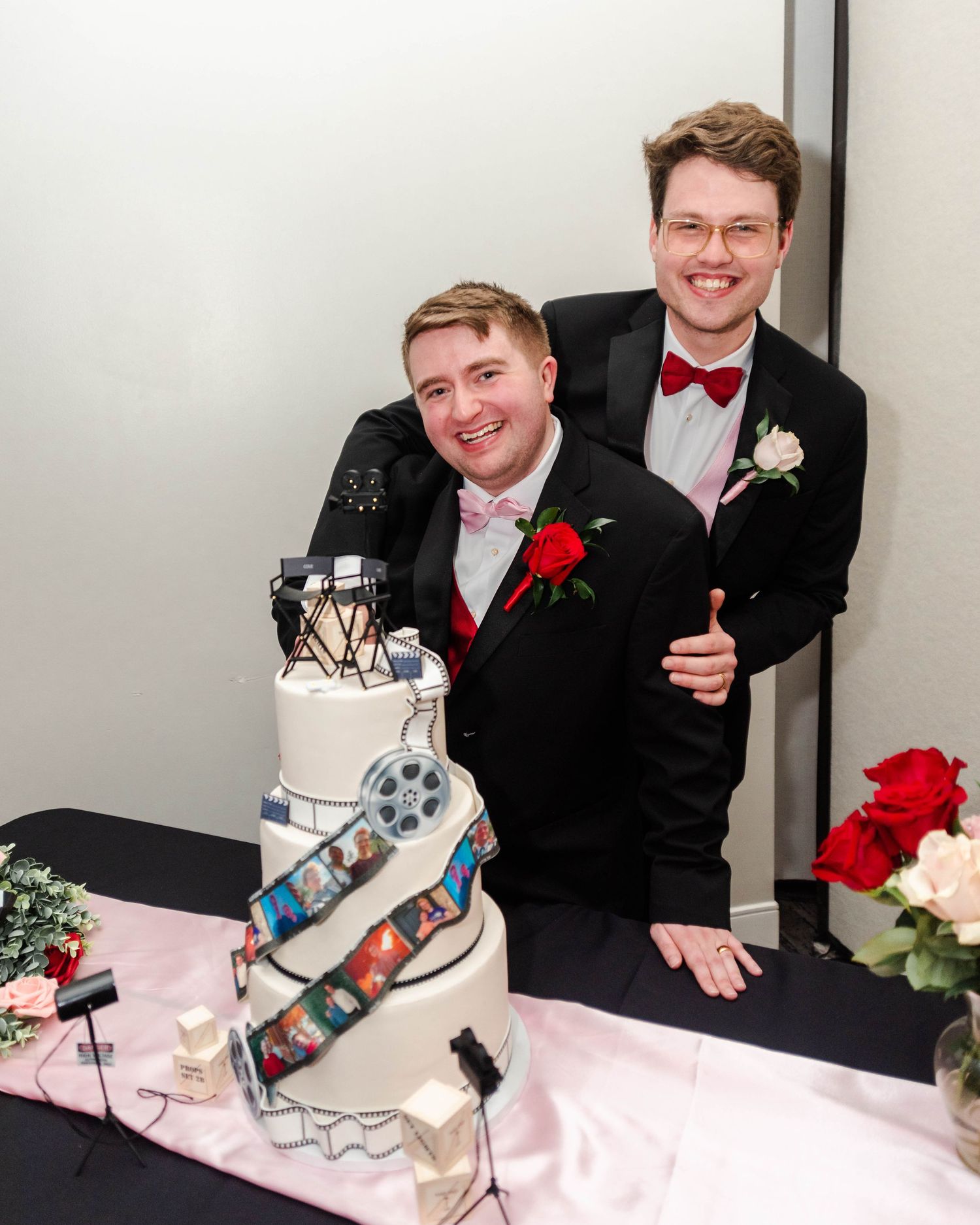 Two gay men are smiling at the camera while next to their wedding cake.