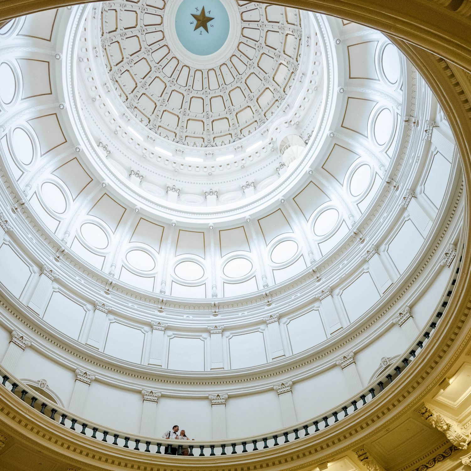 A couple looks up at the ceiling of the Texas State Capitol building where there is a star