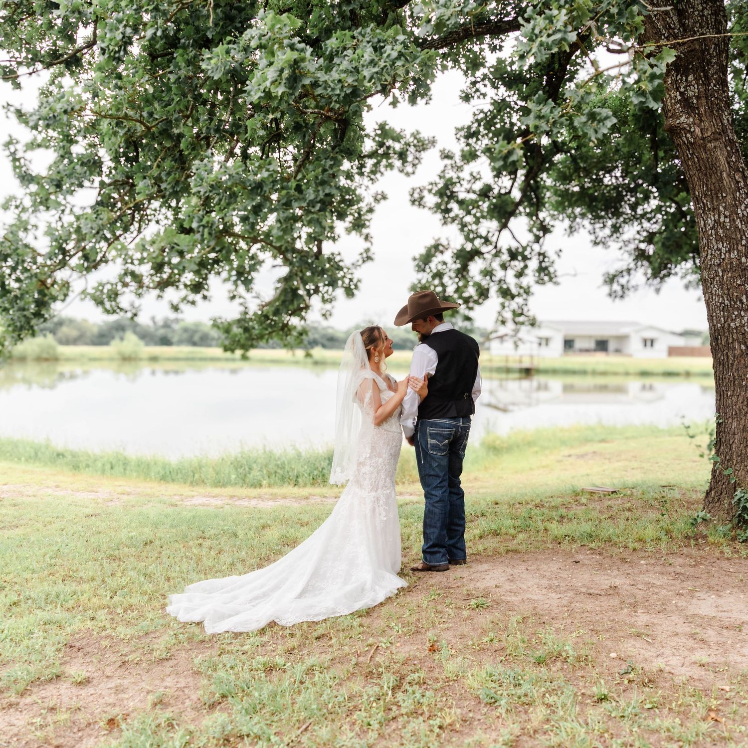A bride and groom look at each other while the bride holds his arm in front of a pond