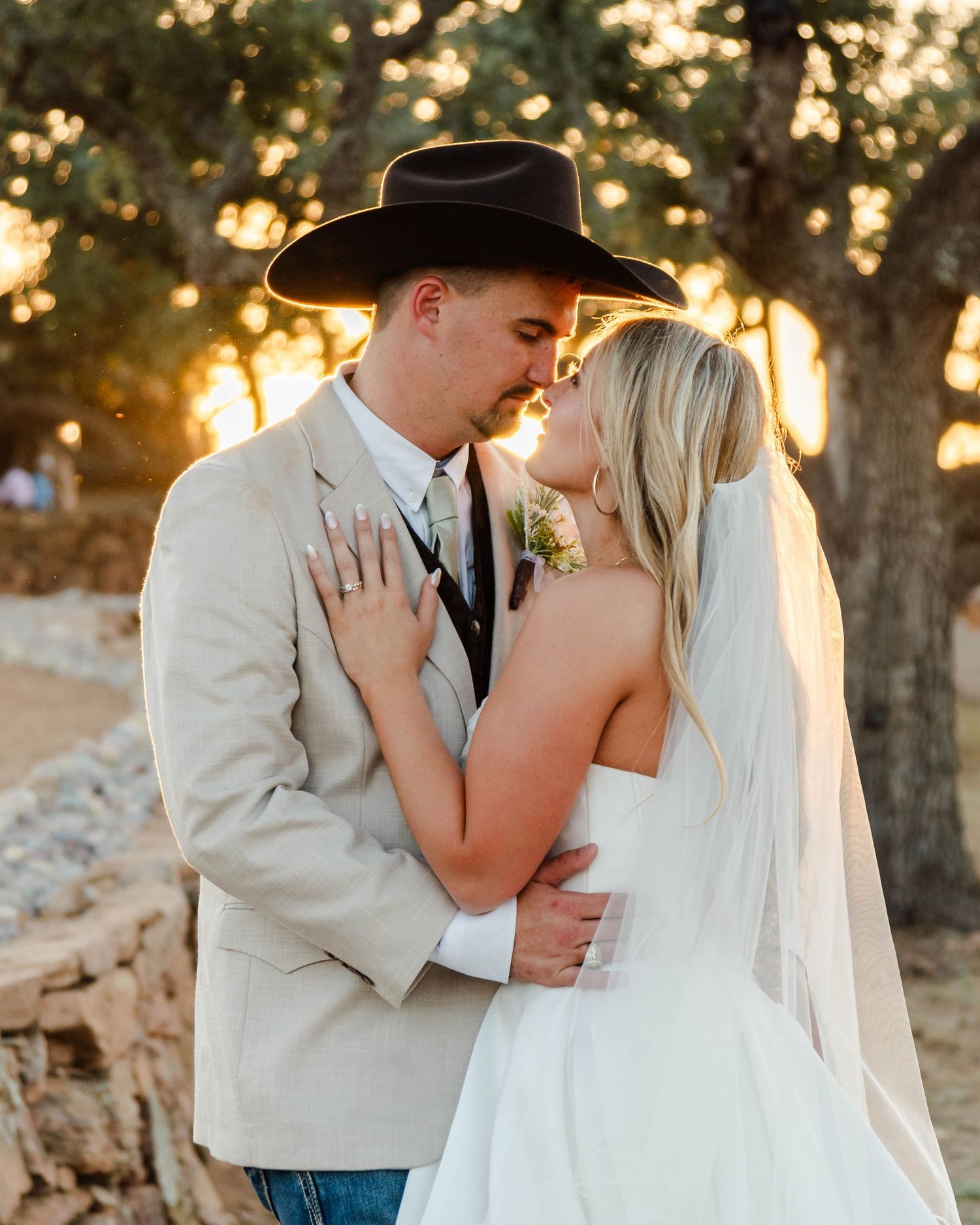 A couple shares a romantic moment at sunset during their western-themed wedding ceremony in an outdoor setting.