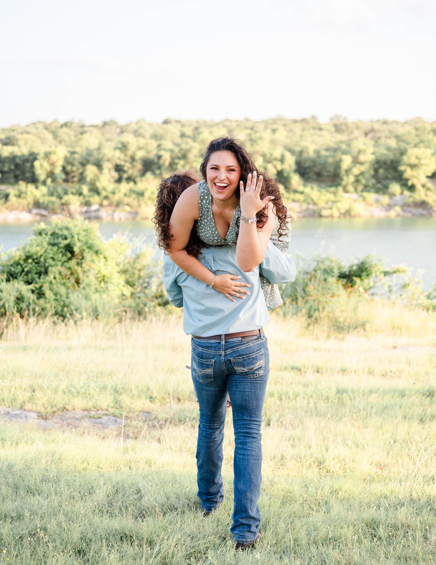 a man carries his fiance away as she smiles and shows off her ring