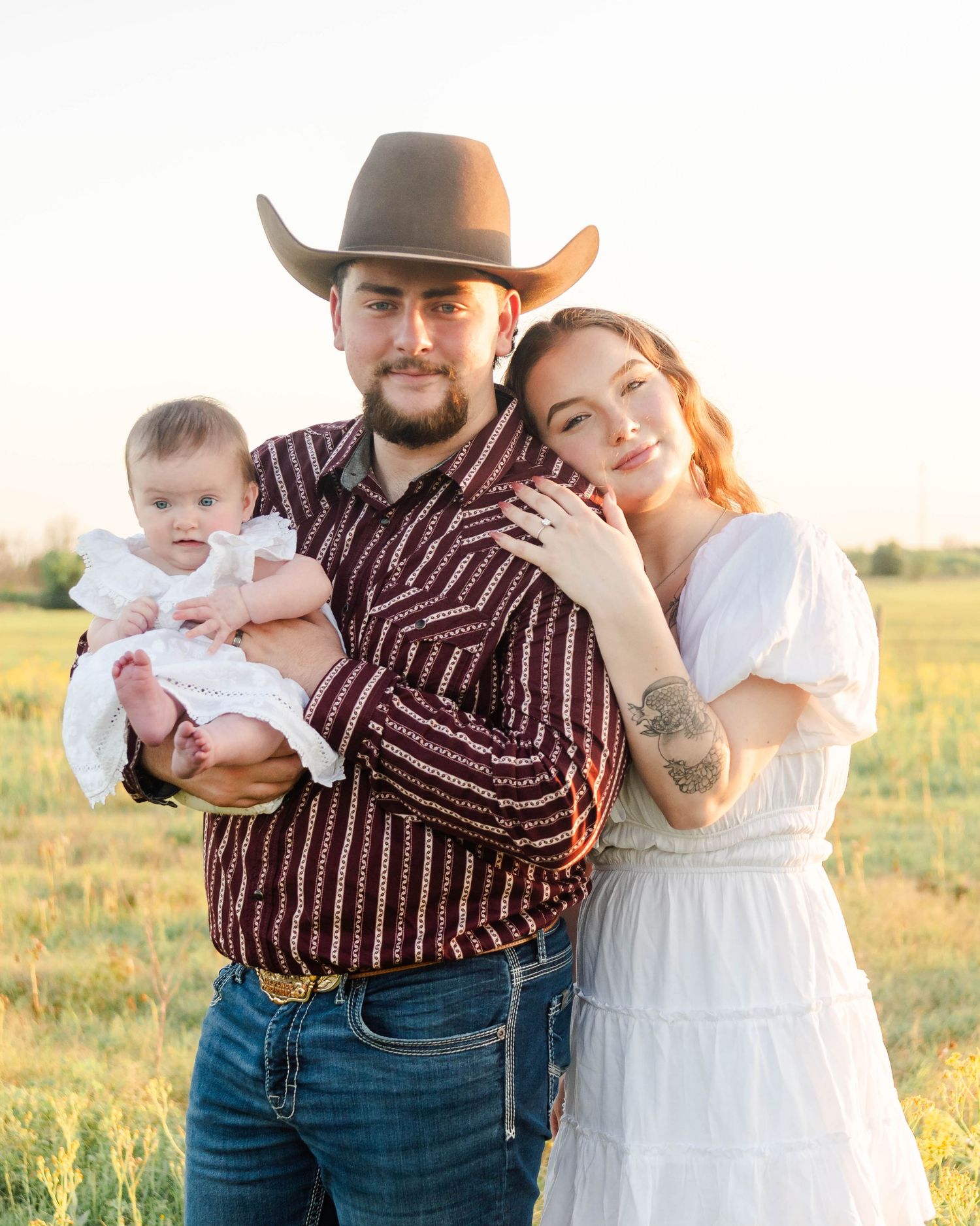a family of three poses while standing in an open pasture