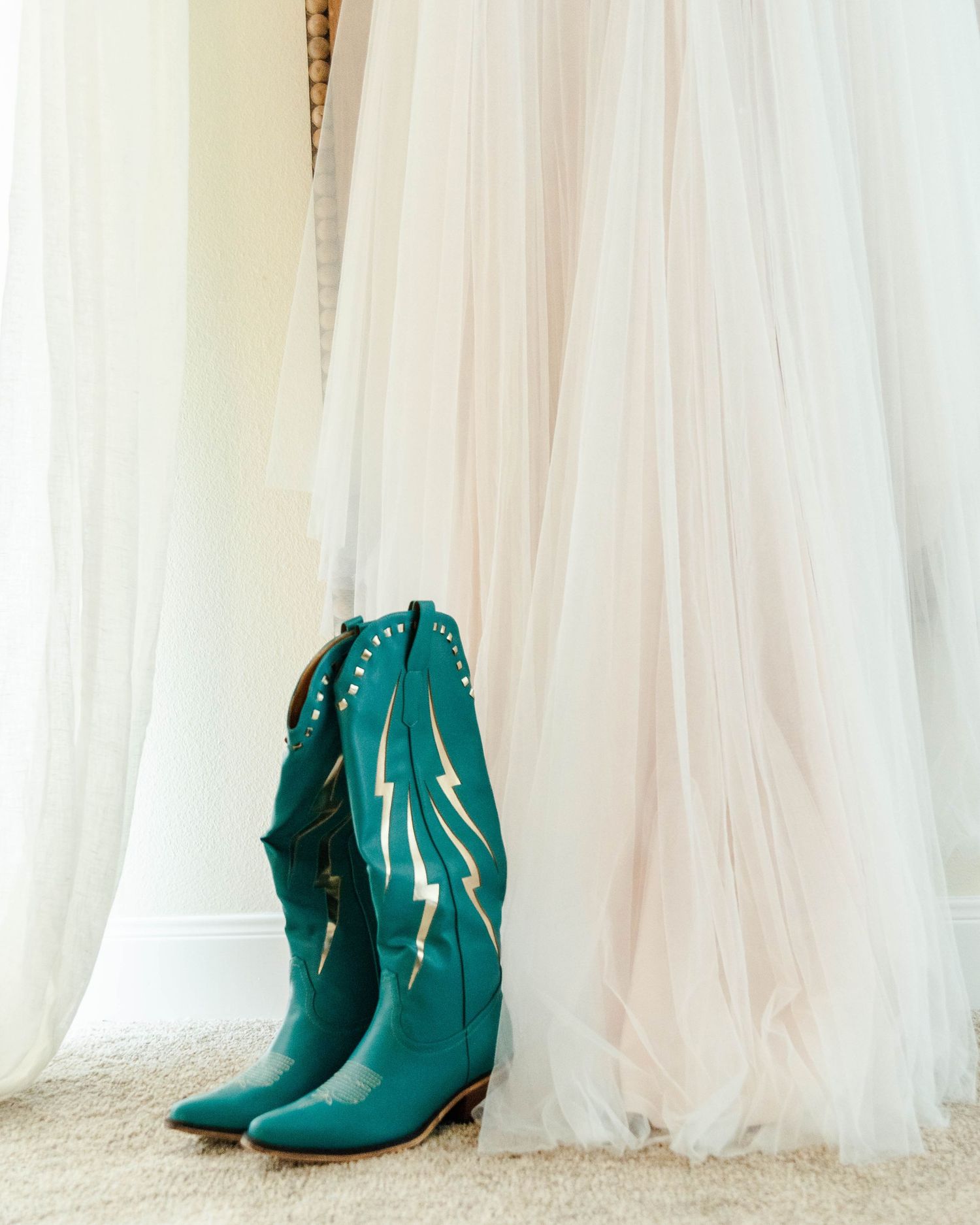 Turquoise studded cowboy boots stand elegantly against flowing white tulle fabric.