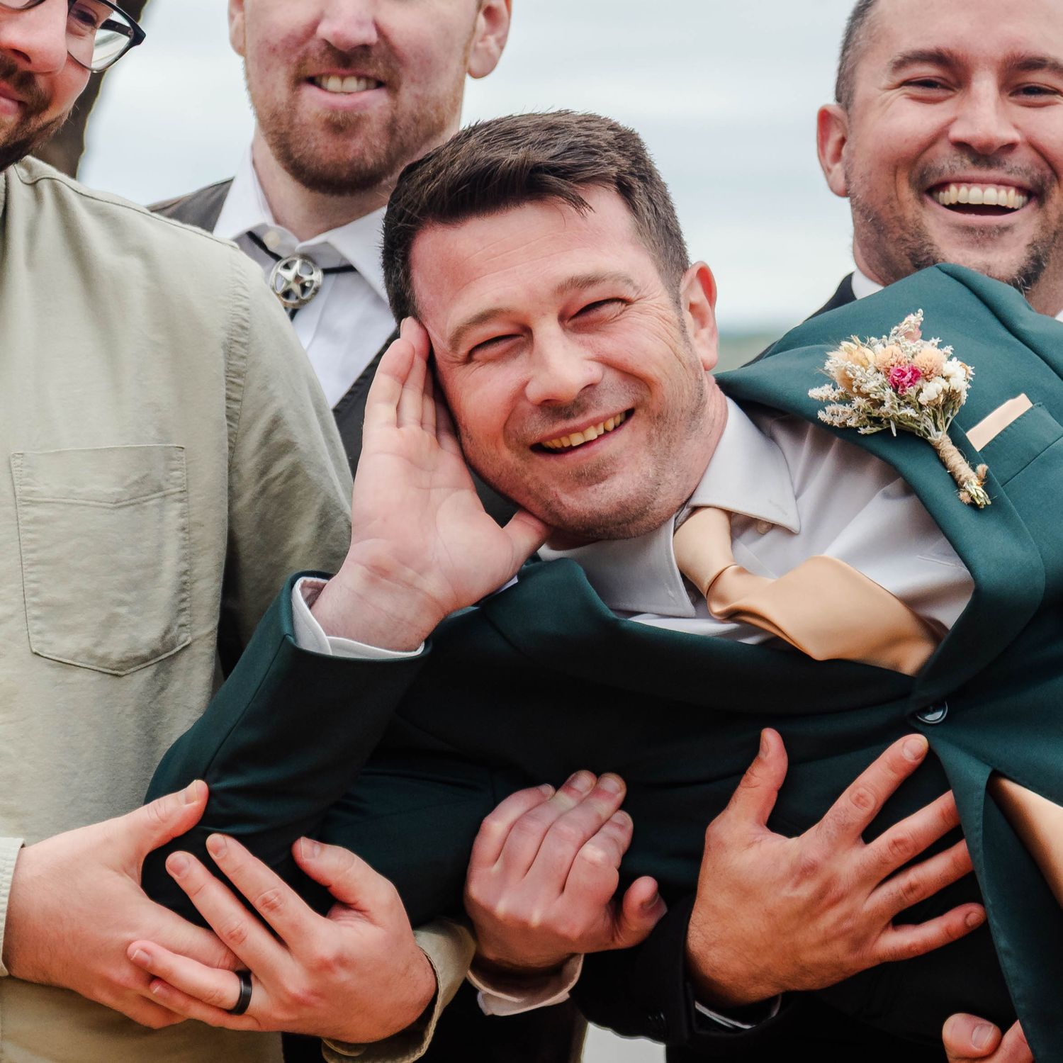 a groom smiling while being held by the groomsmen