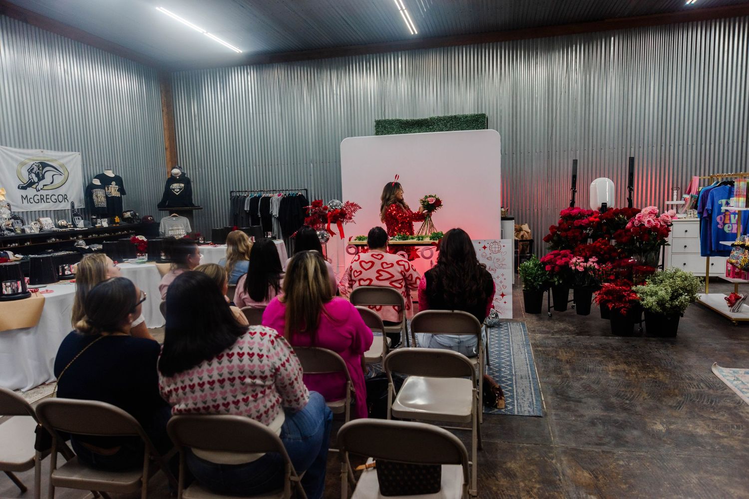 People seated in folding chairs at an indoor event space with poinsettias and holiday decorations visible in the background.