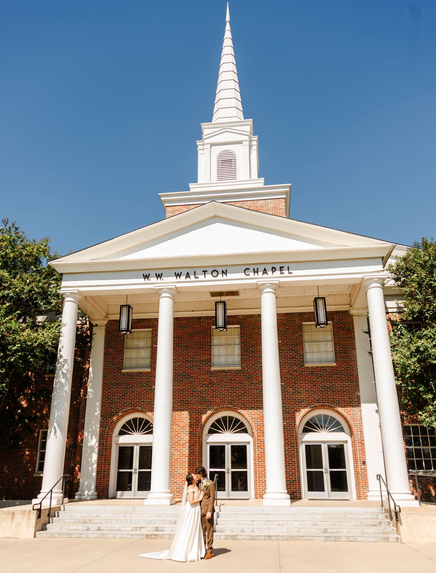 A couple stands in front of a Chapel kissing