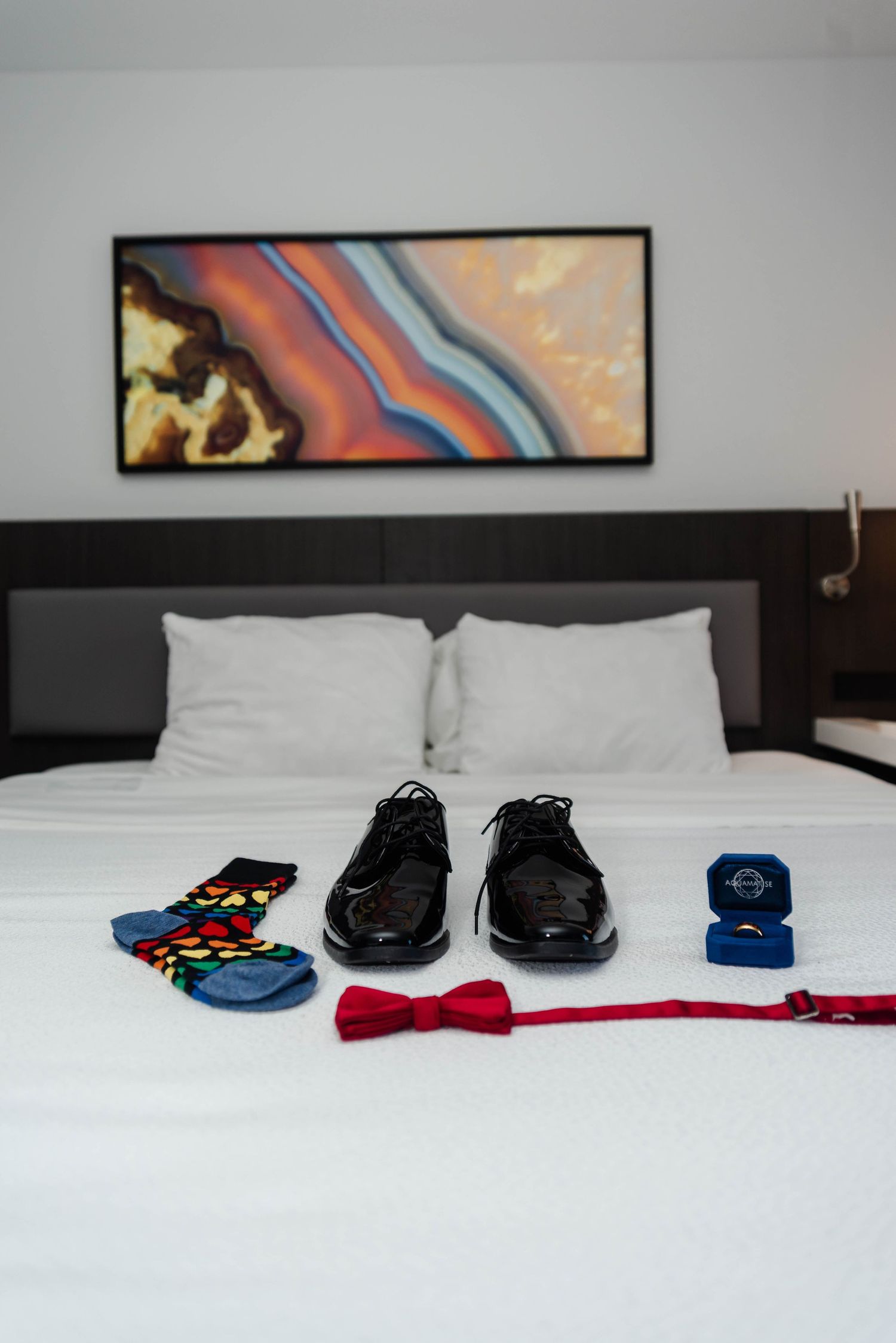 Shoes, wedding ring, bow tie, and socks laid on a hotel bed with white bedding