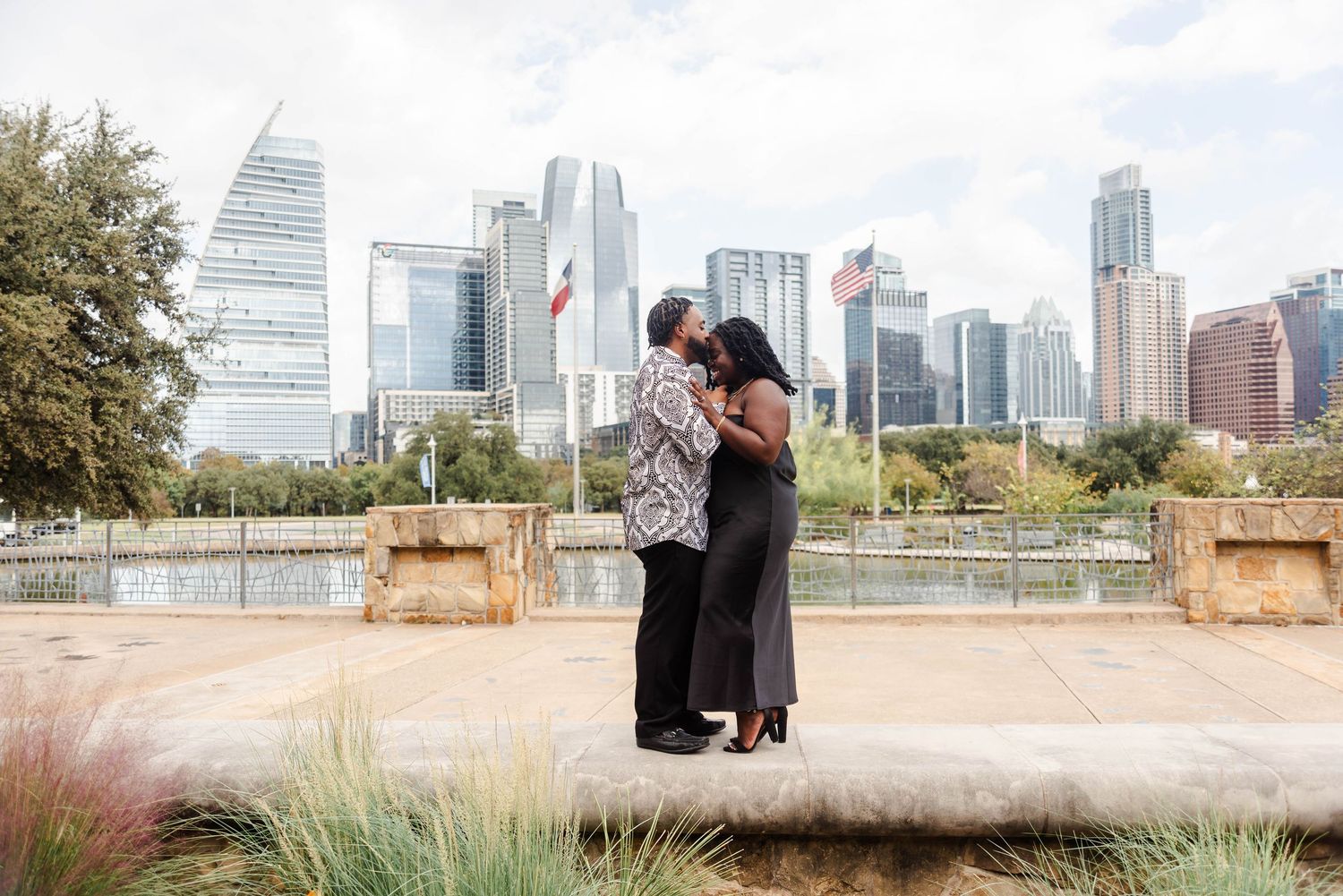 Couple smiles on a sidewalk while the city view is behind them