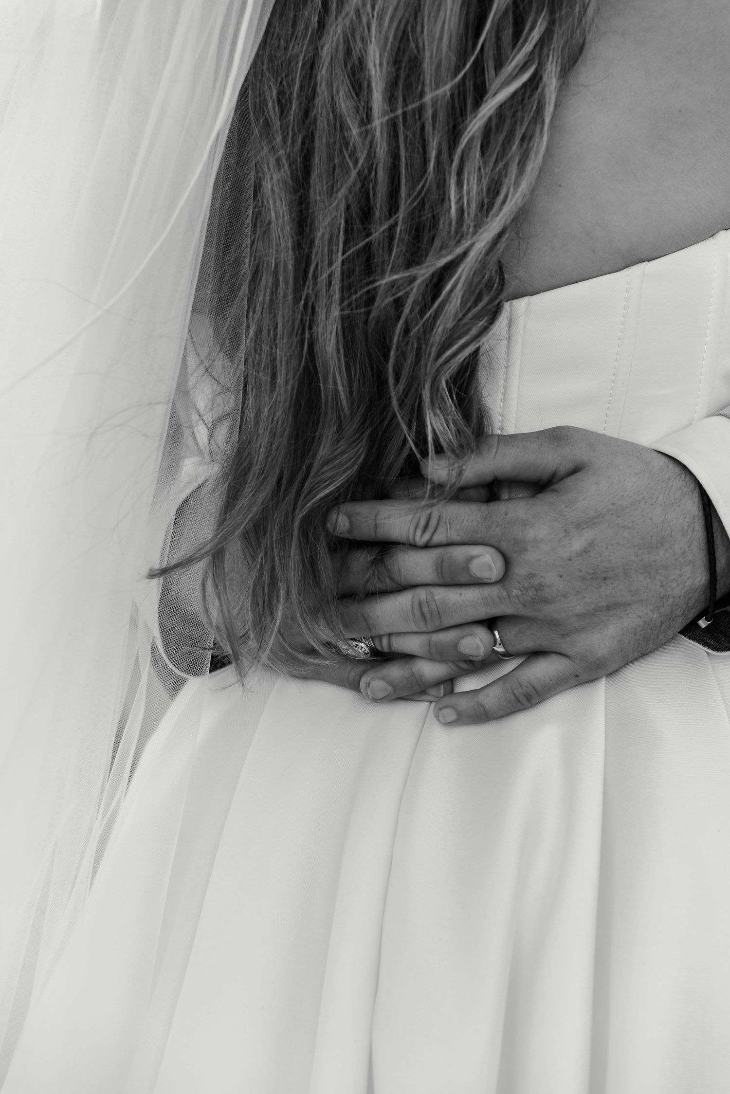 Black and white wedding photo showing a hand with ring resting on long hair and white dress fabric.