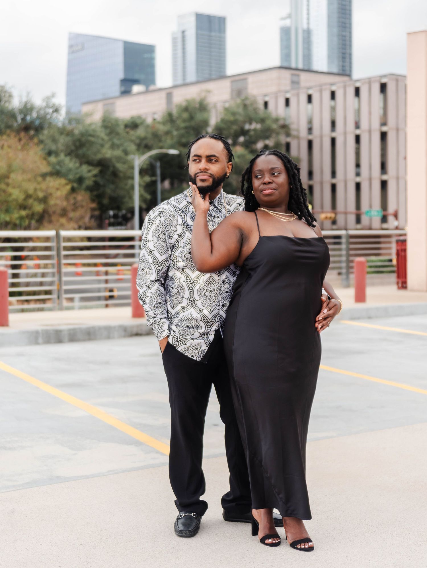 A couple standing on the top level of a parking garage looking off into the distance. The woman is gently holding the mans face.