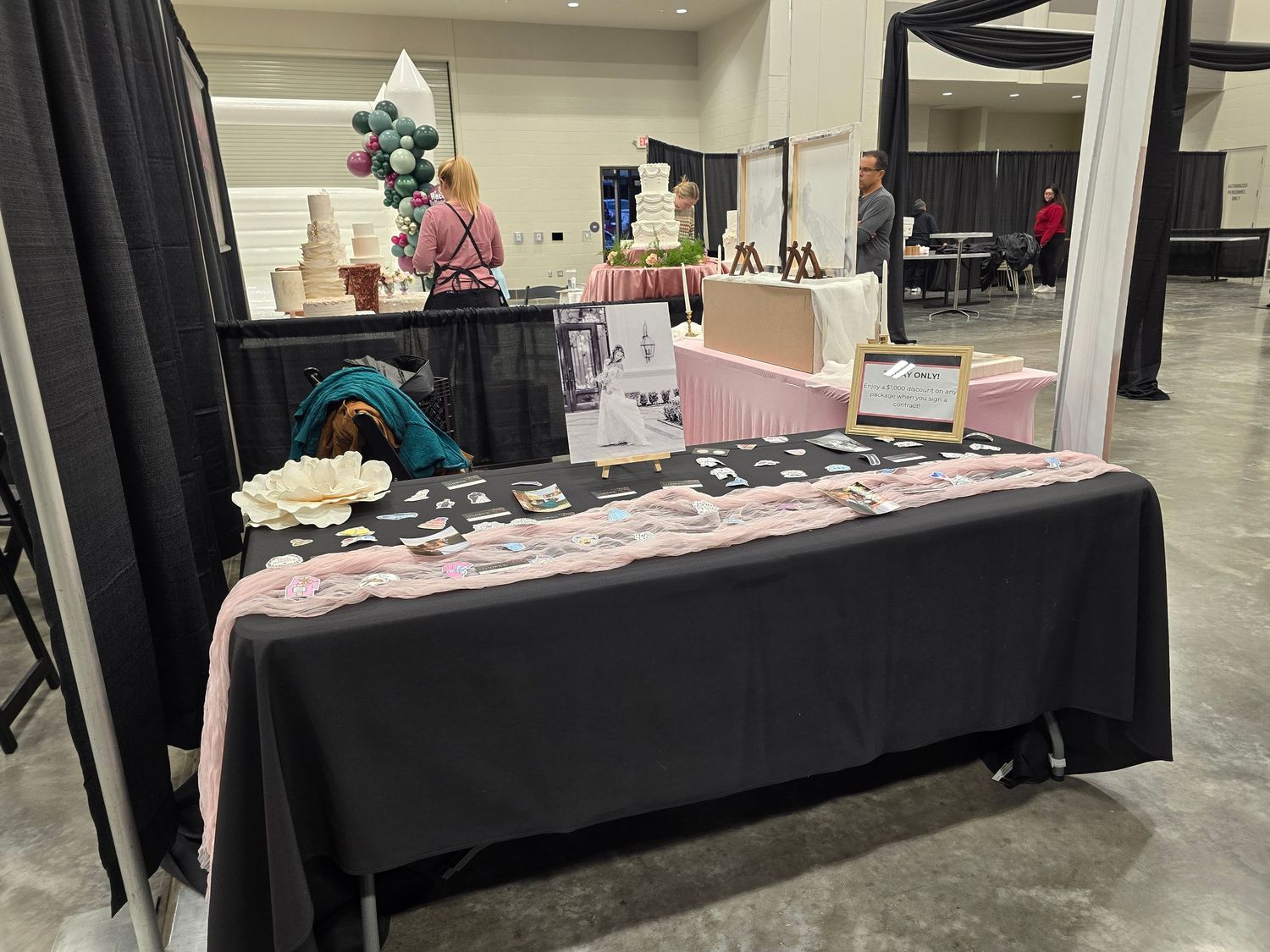 Vendor booth at convention with black tablecloth displaying merchandise and pink accent decor.