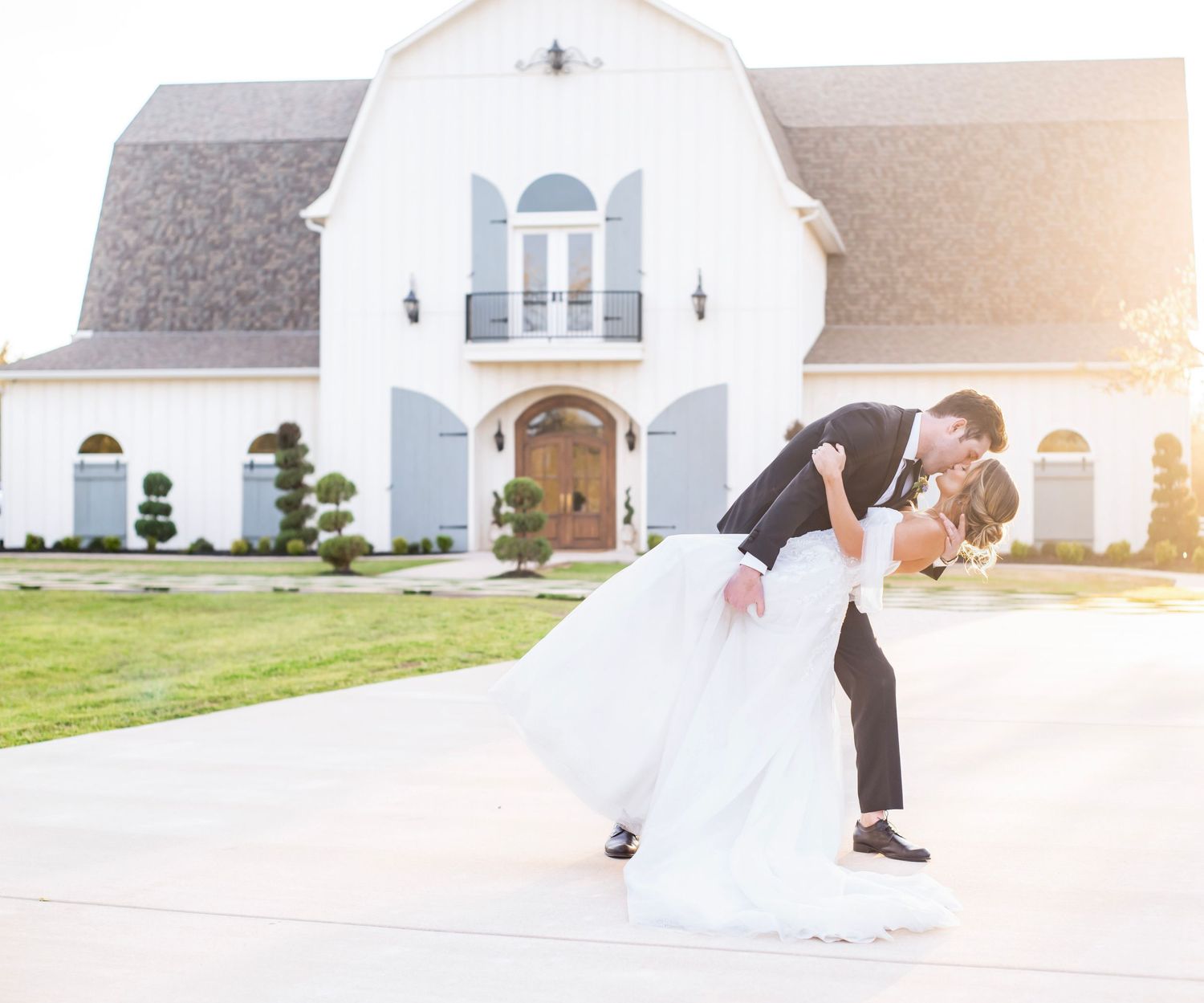 A man dips a woman back for a kiss in front of The French Farmhouse in wedding attire