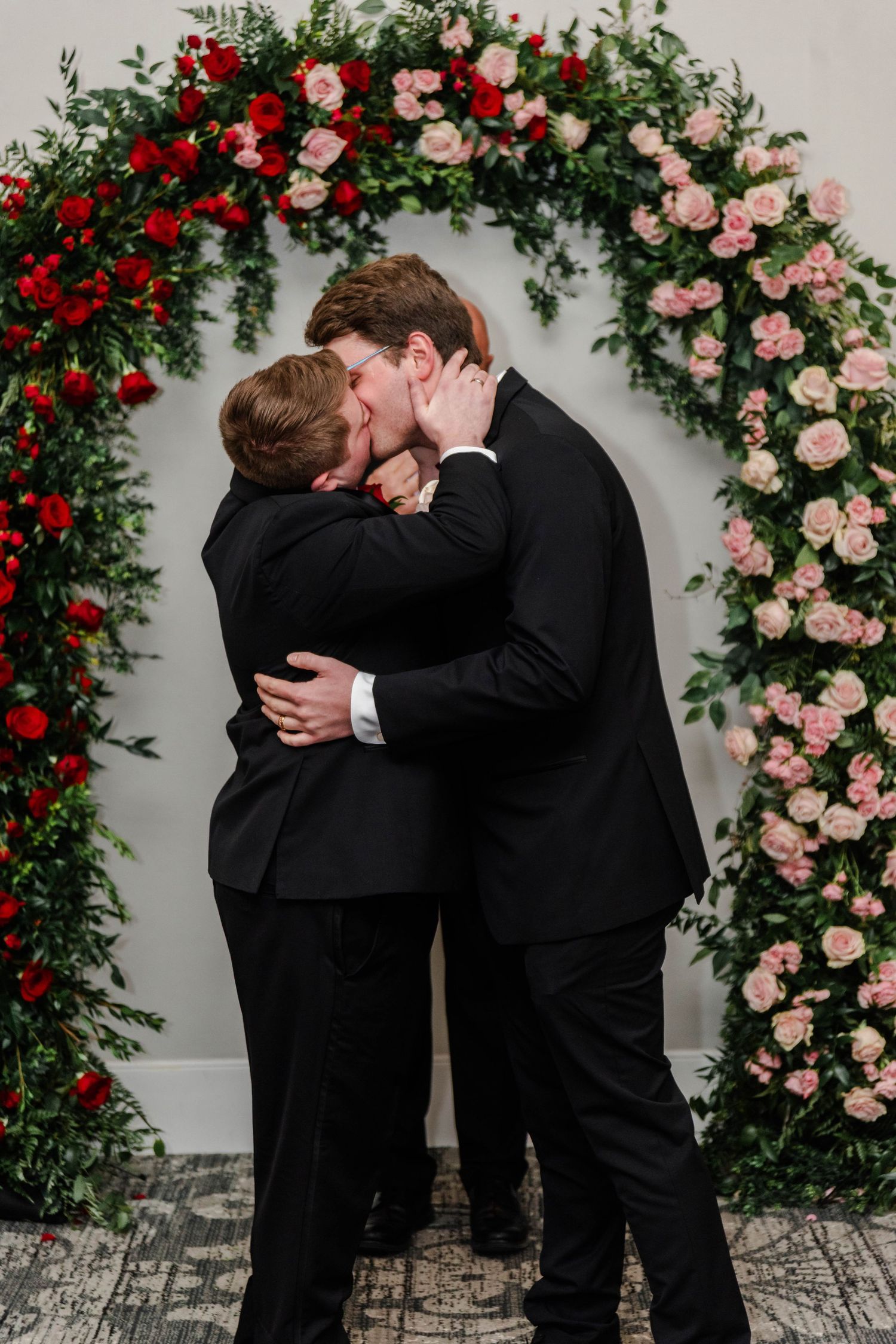 a gay couple kissing at the alter with a flower arch in their tuxedos